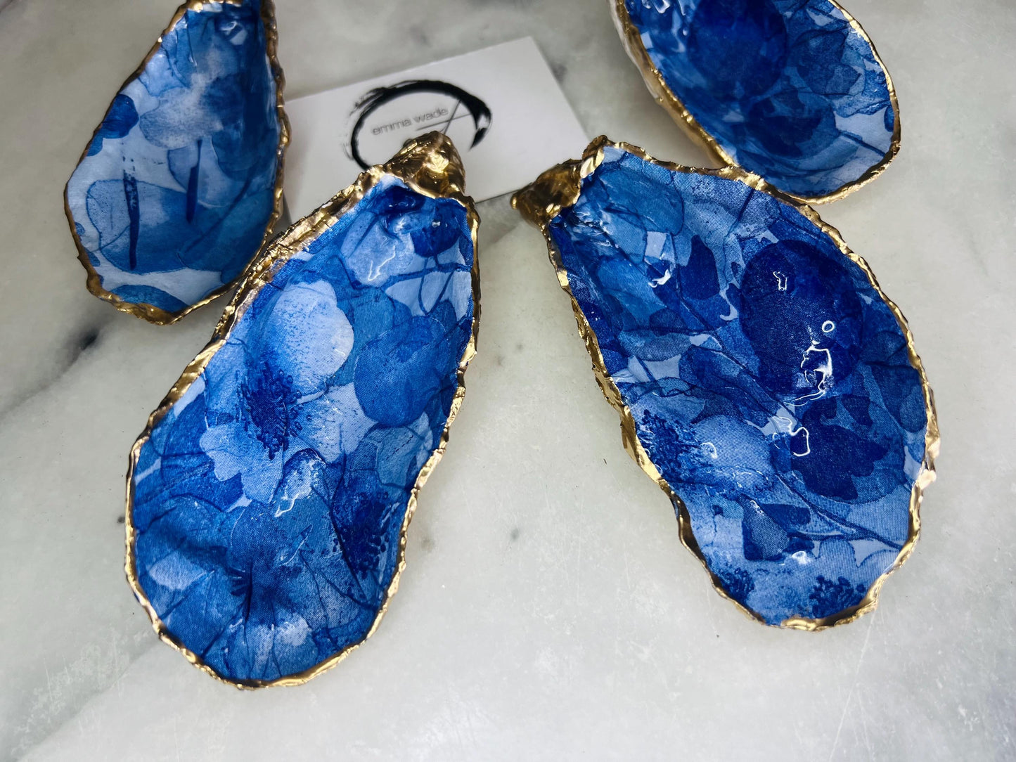 Pair of oyster shell salt and pepper dishes with deep blue watercolour flower design, finished with gold leaf trim and glossy seal. Handmade from Dorset oyster shells, each dish is unique with natural variations. A beautiful oyster shell salt gift set, also available with matching gold crystal spoons for a finishing touch. Perfect for weddings, anniversaries, dinner parties, or as a handmade gift for birthdays, Christmas, or housewarmings. Elegant coastal tableware and decor piece.