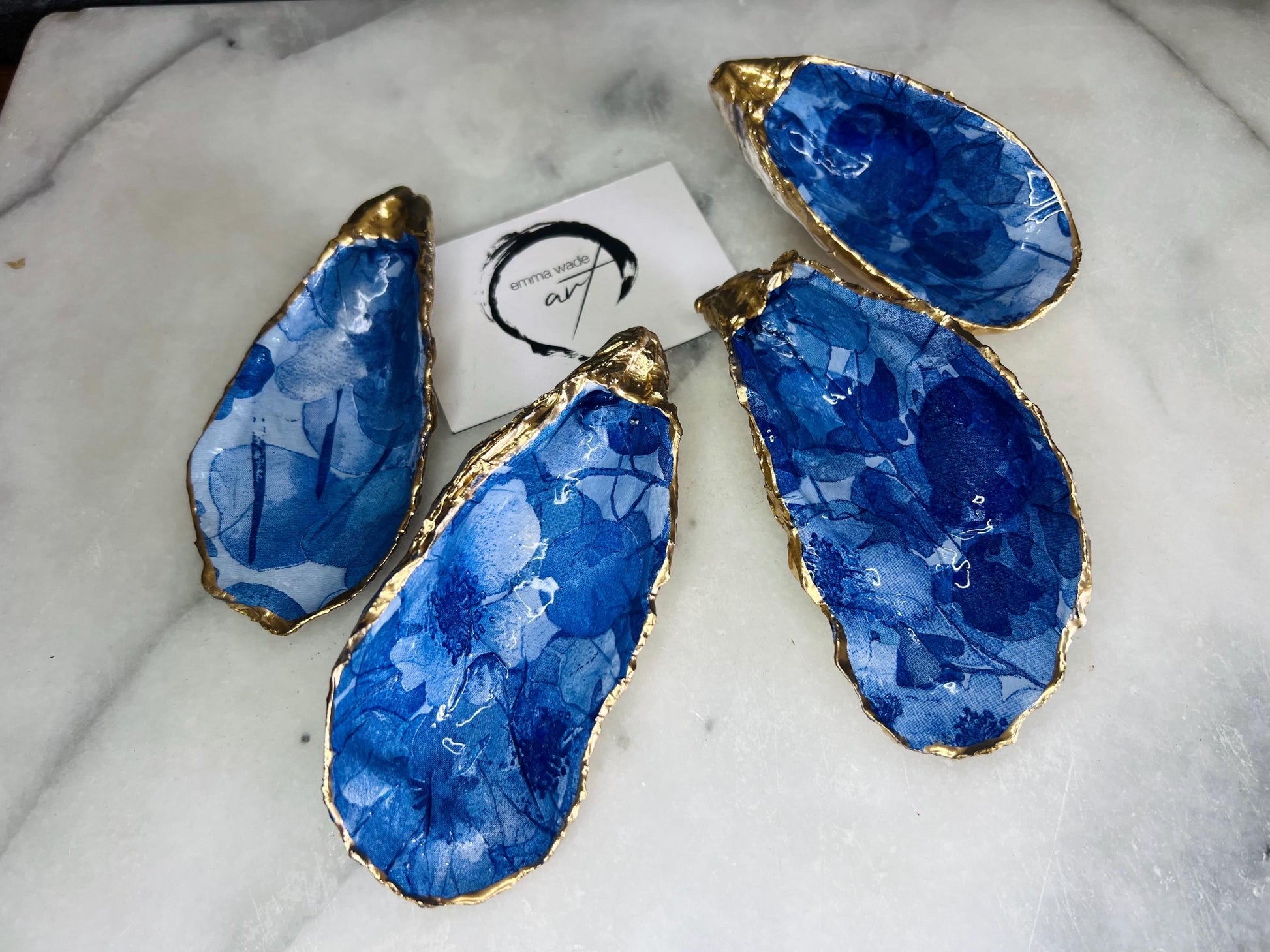 Pair of oyster shell salt and pepper dishes with deep blue watercolour flower design, finished with gold leaf trim and glossy seal. Handmade from Dorset oyster shells, each dish is unique with natural variations. A beautiful oyster shell salt gift set, also available with matching gold crystal spoons for a finishing touch. Perfect for weddings, anniversaries, dinner parties, or as a handmade gift for birthdays, Christmas, or housewarmings. Elegant coastal tableware and decor piece.