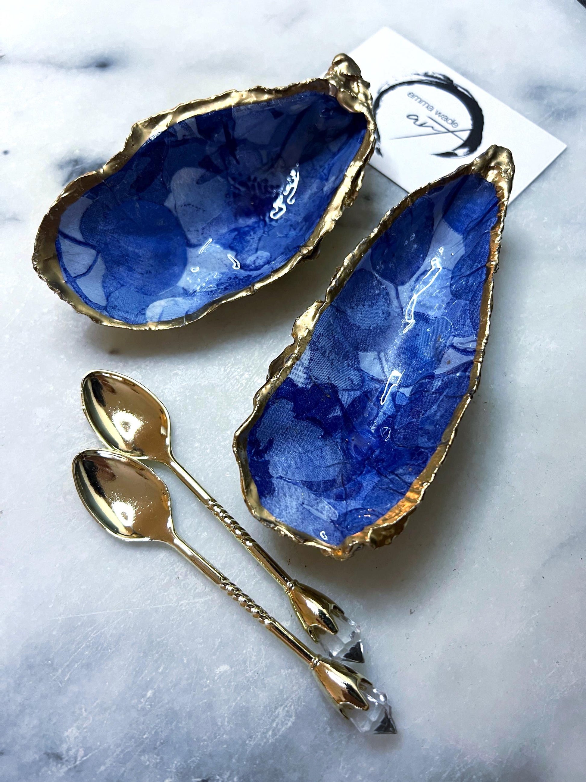 Pair of oyster shell salt and pepper dishes with deep blue watercolour flower design, finished with gold leaf trim and glossy seal. Handmade from Dorset oyster shells, each dish is unique with natural variations. A beautiful oyster shell salt gift set, also available with matching gold crystal spoons for a finishing touch. Perfect for weddings, anniversaries, dinner parties, or as a handmade gift for birthdays, Christmas, or housewarmings. Elegant coastal tableware and decor piece.