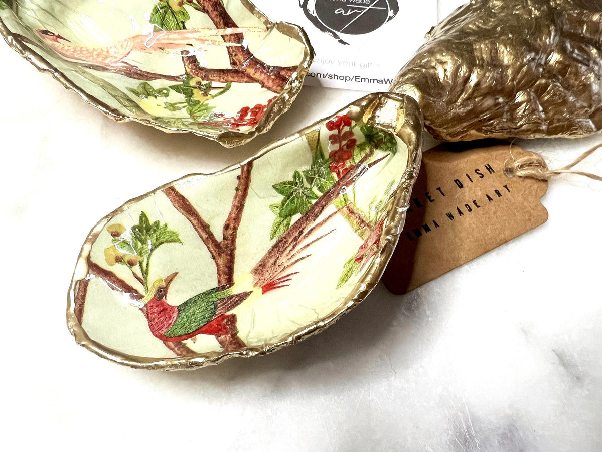Handmade oyster shell trinket dish featuring colourful Bird of Paradise artwork with gold leaf edging and glossy resin finish. Tropical coastal jewellery dish crafted from natural Dorset shells, styled as a ring holder, keepsake tray, or exotic nature-inspired gift.