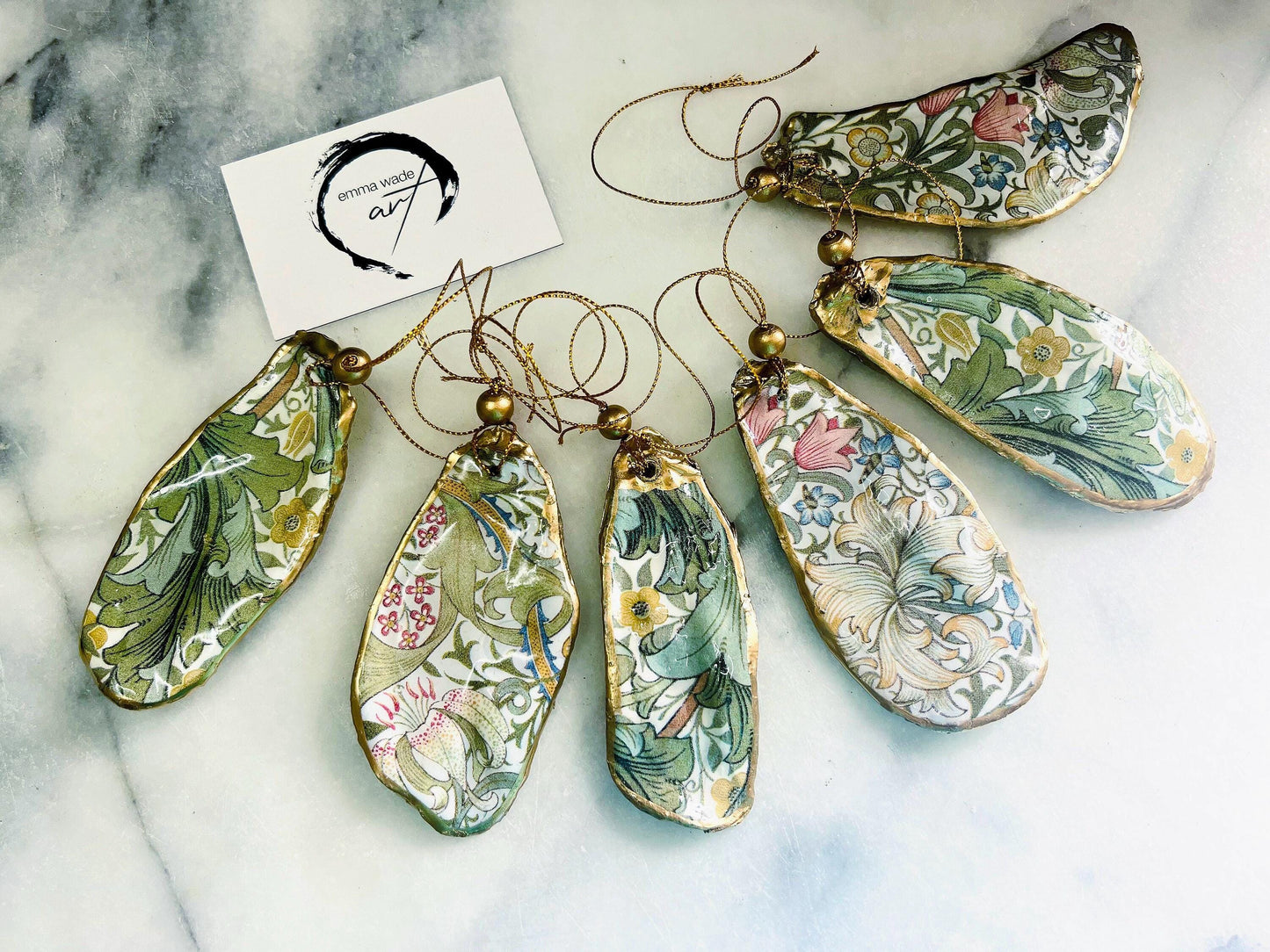 Handmade Dorset oyster shell ornaments decorated with William Morris Gold Granville and Golden Lily designs. Each shell features a natural pearl interior, gold leaf edging, and glossy resin seal. Pre-drilled with gold string and bead for hanging. Options available: individual ornament, matching set of 3, or mixed set of 6. Unique handmade shell decorations perfect for Christmas tree ornaments, wedding favours, bridesmaid gifts, or as William Morris style coastal-inspired home decor.