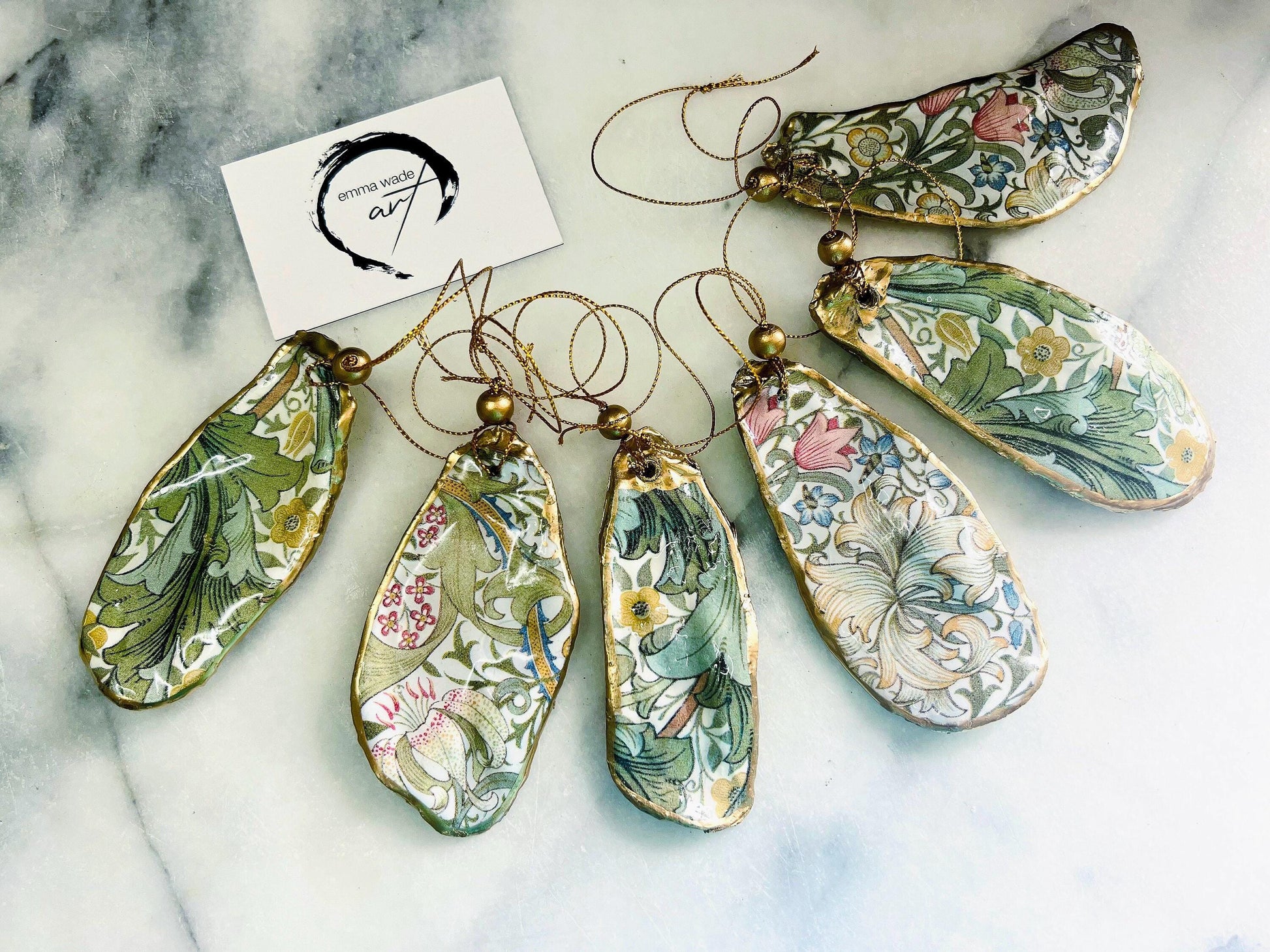Handmade Dorset oyster shell ornaments decorated with William Morris Gold Granville and Golden Lily designs. Each shell features a natural pearl interior, gold leaf edging, and glossy resin seal. Pre-drilled with gold string and bead for hanging. Options available: individual ornament, matching set of 3, or mixed set of 6. Unique handmade shell decorations perfect for Christmas tree ornaments, wedding favours, bridesmaid gifts, or as William Morris style coastal-inspired home decor.