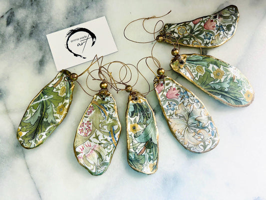 Handmade Dorset oyster shell ornaments decorated with William Morris Gold Granville and Golden Lily designs. Each shell features a natural pearl interior, gold leaf edging, and glossy resin seal. Pre-drilled with gold string and bead for hanging. Options available: individual ornament, matching set of 3, or mixed set of 6. Unique handmade shell decorations perfect for Christmas tree ornaments, wedding favours, bridesmaid gifts, or as William Morris style coastal-inspired home decor.