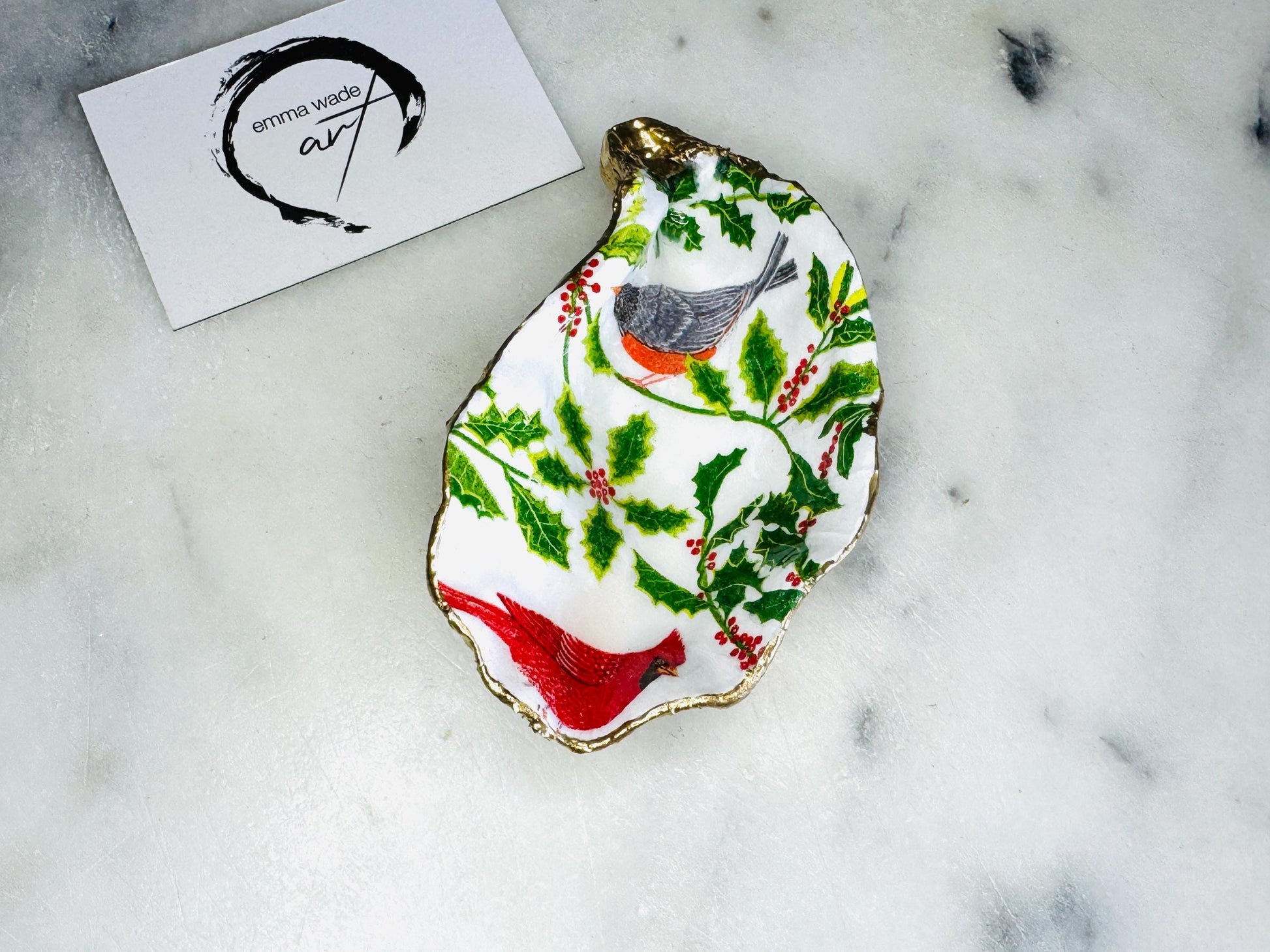 Handmade Dorset oyster shell Christmas ornament featuring red and orange winter birds perched amongst festive green foliage and berries. Coastal oyster shell trinket dish with hand applied gold leaf edging and glossy resin finish, styled as luxury Christmas décor. Sustainable handcrafted robin-inspired shell decoration available as hanging ornament or jewellery dish, inspired by British winter wildlife and the Dorset coastline.