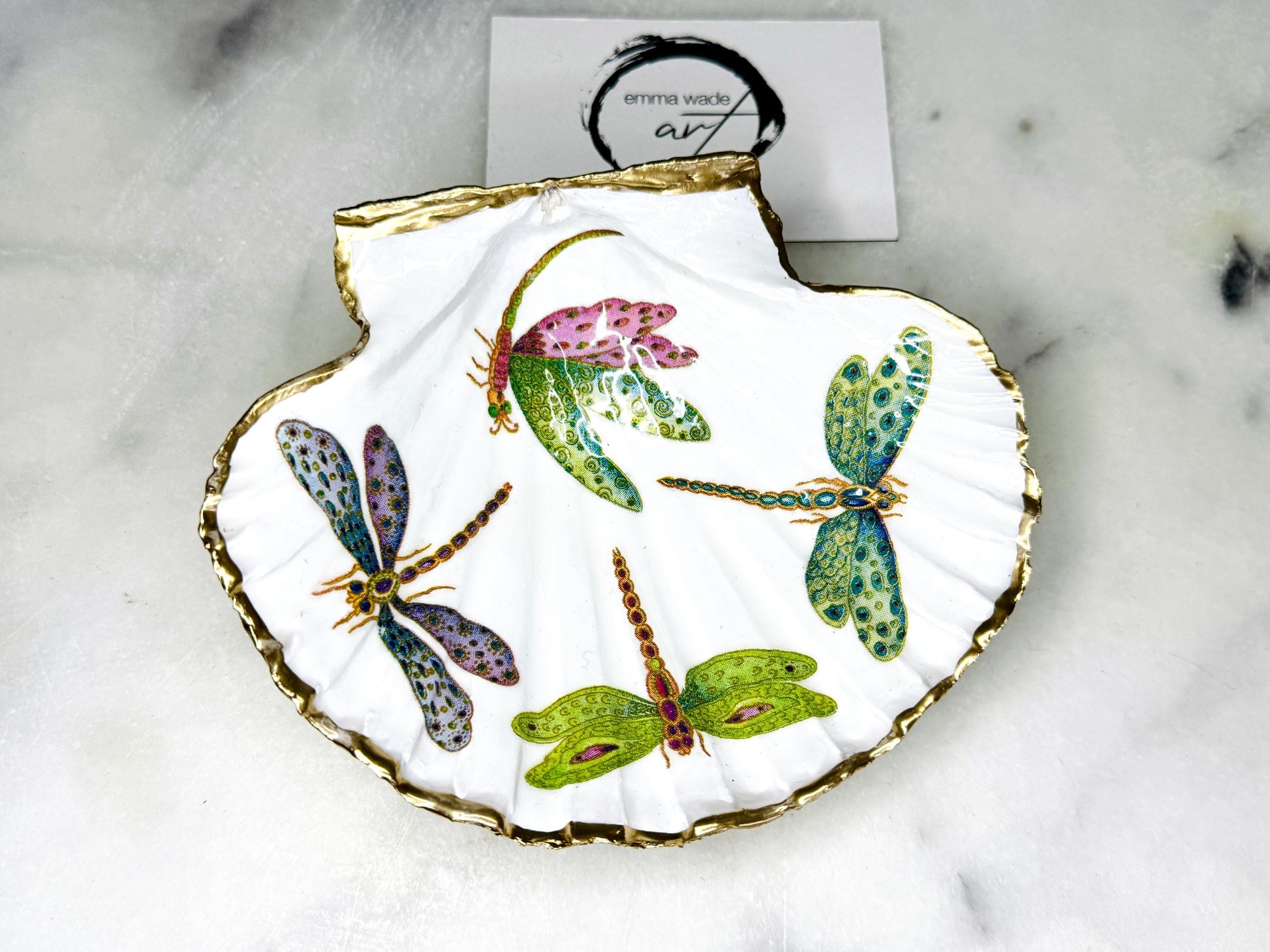 Handmade dragonfly scallop shell trinket dish with gold leaf edging and glossy resin finish. Coastal jewellery and ring dish crafted from a natural Dorset scallop shell, featuring colourful dragonfly artwork. Decorative shell bowl photographed on a light background, showing the natural shell shape and shimmering gilded edges, ideal for holding rings, earrings, trinkets or small treasures.