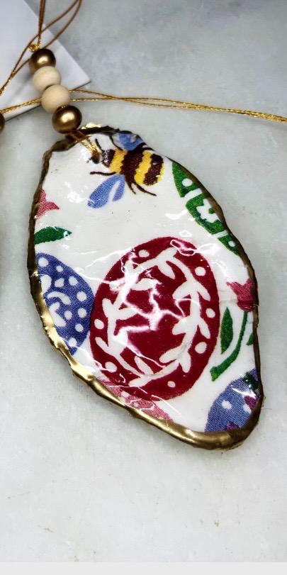 Handmade Dorset oyster shell ornaments featuring Emma Bridgewater bee, butterfly, and egg designs. Each shell has a natural pearl finish, gilded with liquid gold leaf on the rim and back, and sealed with glossy resin for shine and durability. Available individually or as a set of 3, with pre-drilled holes, gold hanging string, and decorative beads. Unique festive decorations for Christmas trees, seasonal home décor, or handmade coastal-inspired gifts for weddings, birthdays, or anniversaries.