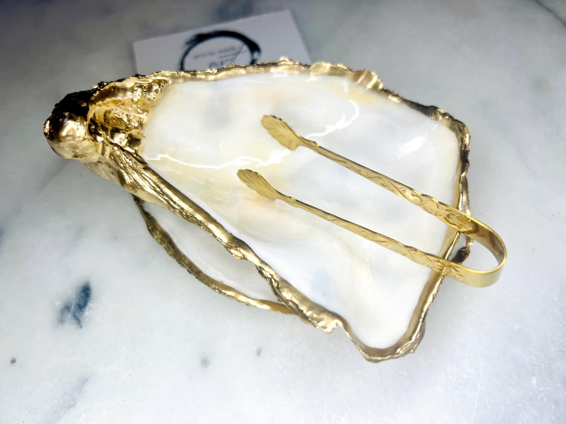 Extra large Dorset oyster shell serving dish set with natural pearl interior and hand-applied gold leaf edging, featuring a cupped XL oyster shell with matching flat shell base. Luxury coastal home décor ideal as a sugar dish, serving bowl, coffee station accessory, or elegant host gift. Handmade using sustainably sourced UK oyster shells and finished with glossy resin and optional gold serving accessories.