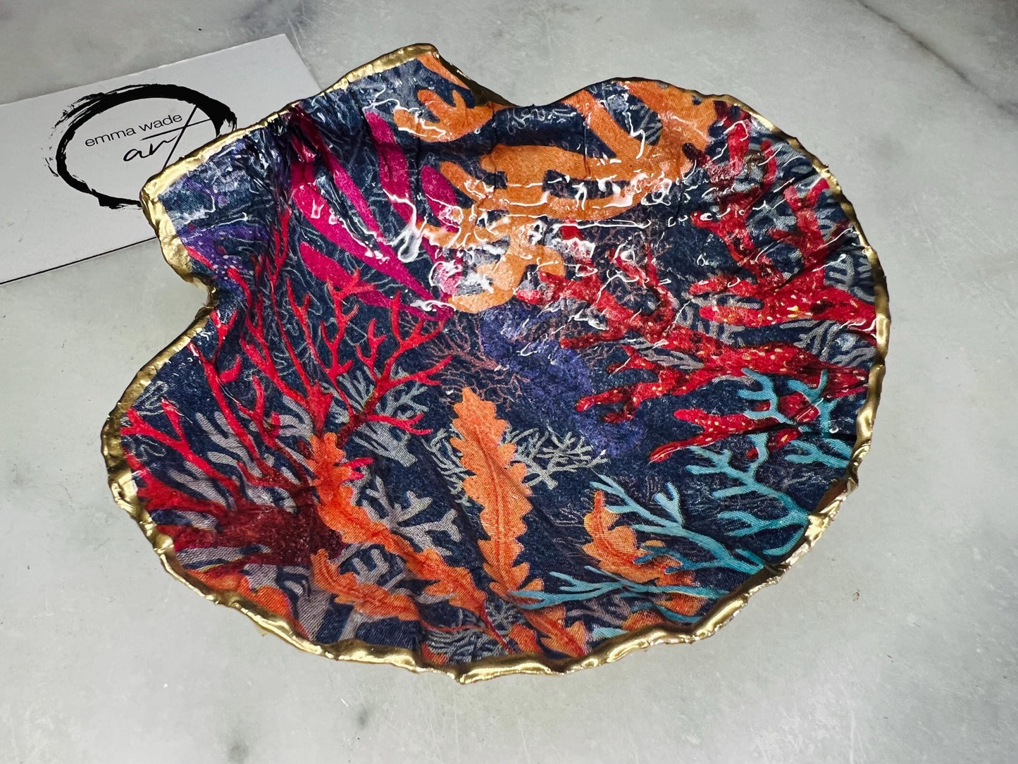 Handmade Dorset scallop shell trinket dish featuring vibrant coral reef and seaweed design in red orange turquoise and navy blue tones, finished with hand gilded gold leaf edging and glossy resin, luxury coastal jewellery holder and ocean inspired decor