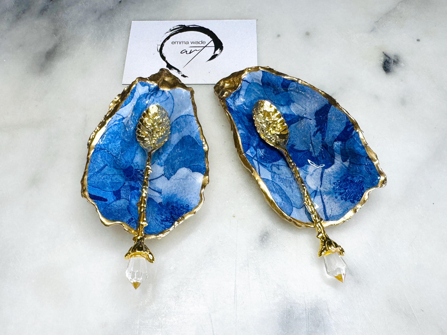 Pair of oyster shell salt and pepper dishes with deep blue watercolour flower design, finished with gold leaf trim and glossy seal. Handmade from Dorset oyster shells, each dish is unique with natural variations. A beautiful oyster shell salt gift set, also available with matching gold crystal spoons for a finishing touch. Perfect for weddings, anniversaries, dinner parties, or as a handmade gift for birthdays, Christmas, or housewarmings. Elegant coastal tableware and decor piece.