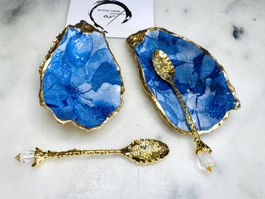 Pair of oyster shell salt and pepper dishes with deep blue watercolour flower design, finished with gold leaf trim and glossy seal. Handmade from Dorset oyster shells, each dish is unique with natural variations. A beautiful oyster shell salt gift set, also available with matching gold crystal spoons for a finishing touch. Perfect for weddings, anniversaries, dinner parties, or as a handmade gift for birthdays, Christmas, or housewarmings. Elegant coastal tableware and decor piece.