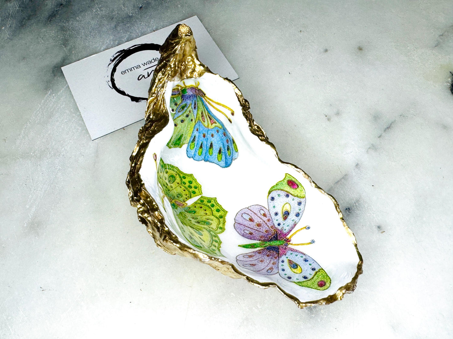 Handmade butterfly oyster shell trinket dish with colourful blue green and pink butterfly designs, edged and backed in gold leaf, Dorset coastal shell jewellery holder with glossy resin finish, luxury ring dish, coastal home decor gift, unique handmade shell dish for jewellery storage, beach house accessory, UK artisan oyster shell dish