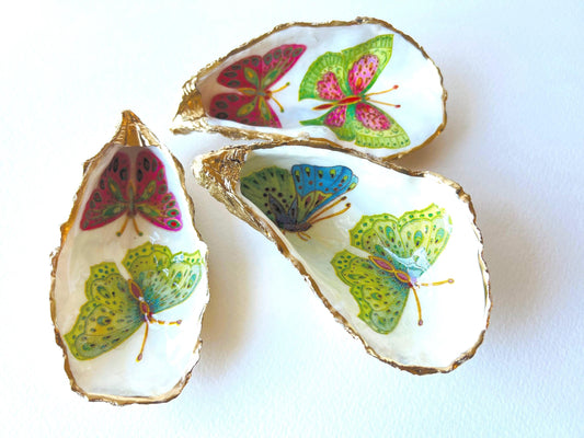 Handmade butterfly oyster shell trinket dish with colourful blue green and pink butterfly designs, edged and backed in gold leaf, Dorset coastal shell jewellery holder with glossy resin finish, luxury ring dish, coastal home decor gift, unique handmade shell dish for jewellery storage, beach house accessory, UK artisan oyster shell dish