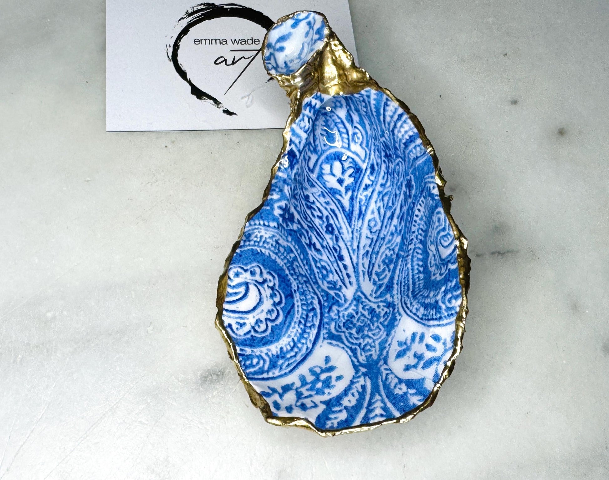 Handmade Dorset oyster shell trinket dish featuring an elegant blue and white paisley design, hand-gilded with liquid gold leaf and finished in glossy resin. Coastal shell jewellery holder available in multiple sizes from small to XL, ideal as a ring dish, trinket tray, vanity decor, or luxury coastal gift.