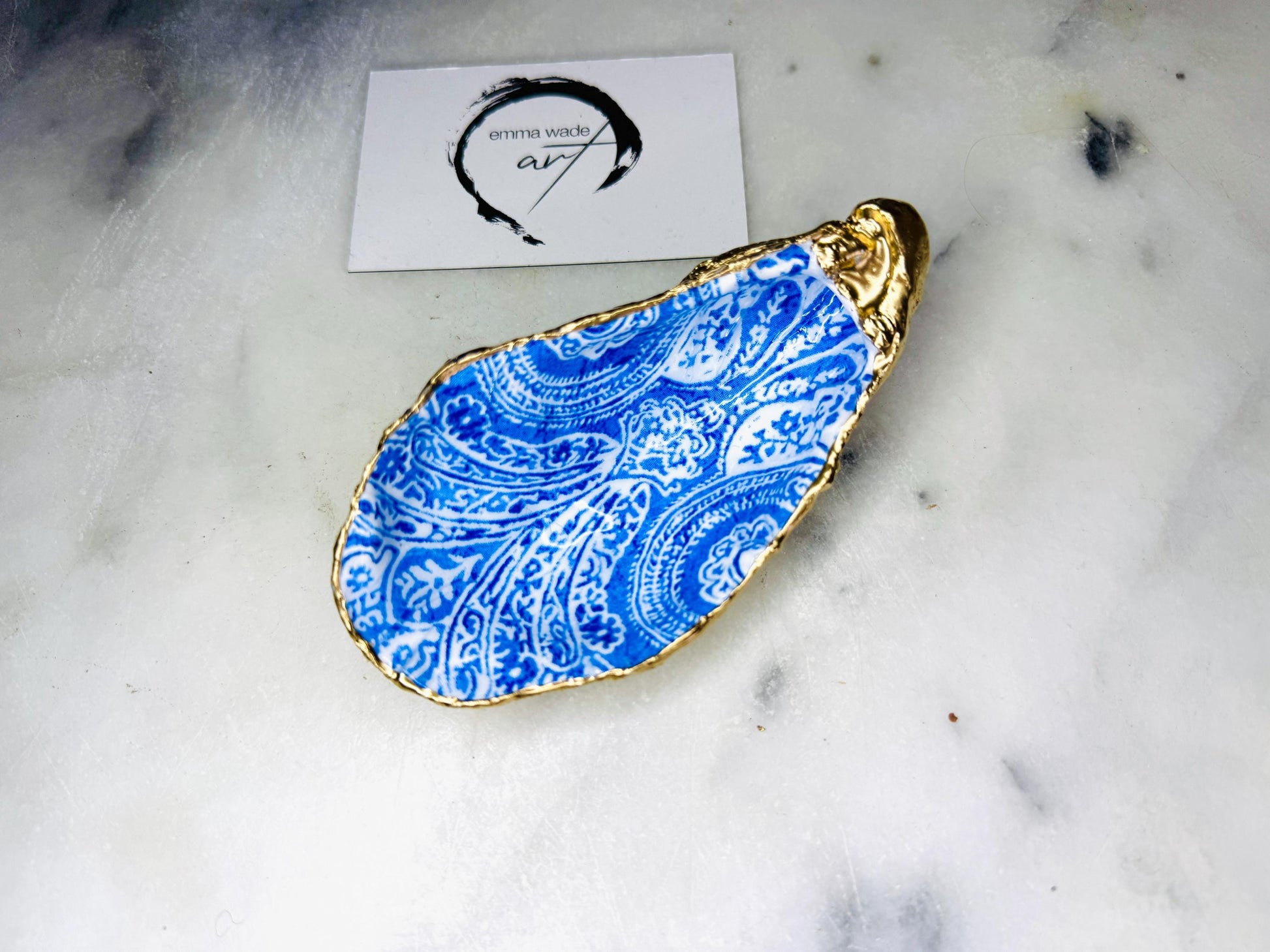 Handmade Dorset oyster shell trinket dish featuring an elegant blue and white paisley design, hand-gilded with liquid gold leaf and finished in glossy resin. Coastal shell jewellery holder available in multiple sizes from small to XL, ideal as a ring dish, trinket tray, vanity decor, or luxury coastal gift.