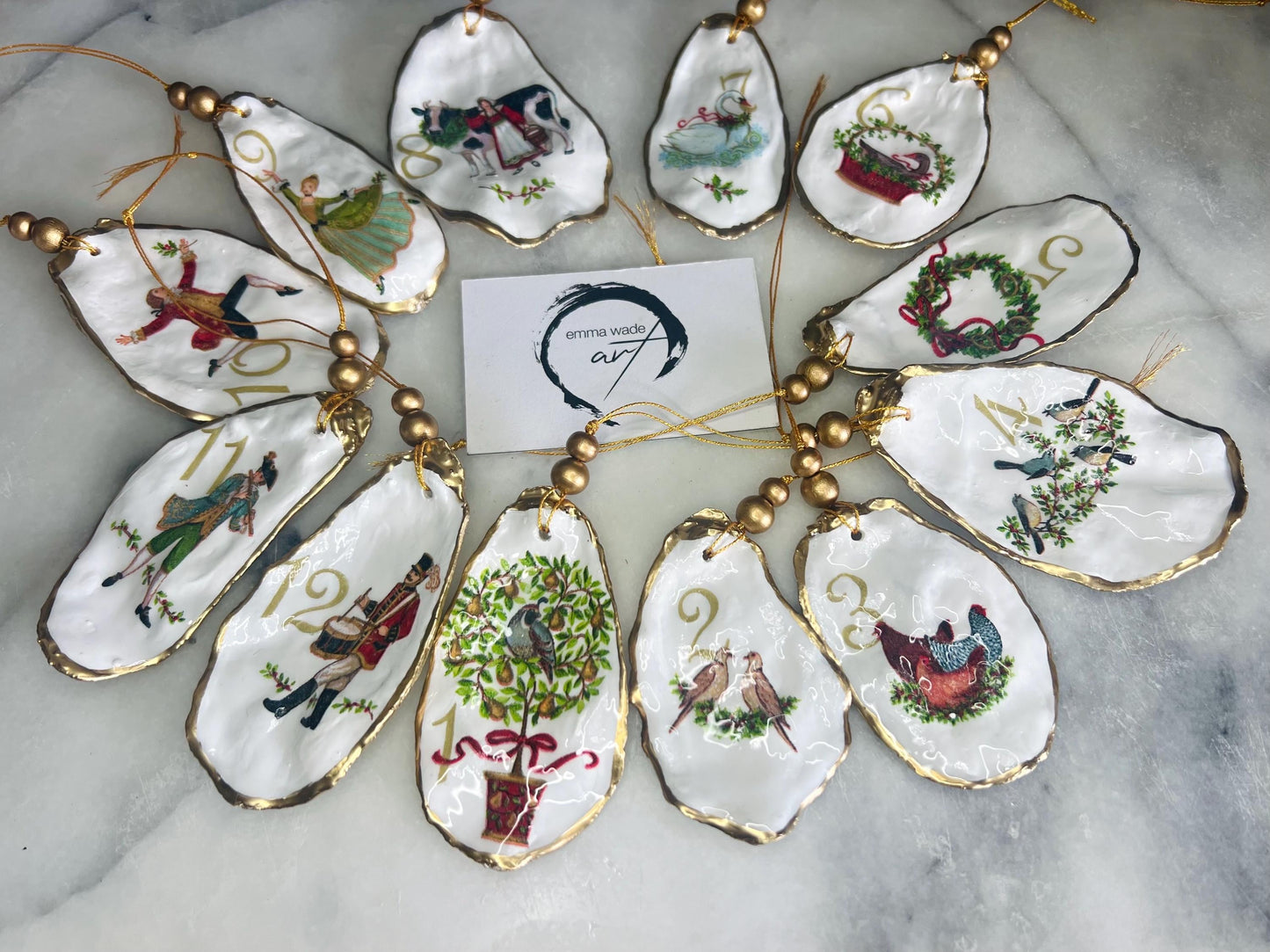 Handmade Twelve Days of Christmas oyster shell ornament set featuring all twelve traditional carol illustrations, finished with gold leaf edging, glossy resin and gold hanging cords. Coastal heirloom Christmas decorations handcrafted from Dorset oyster shells.