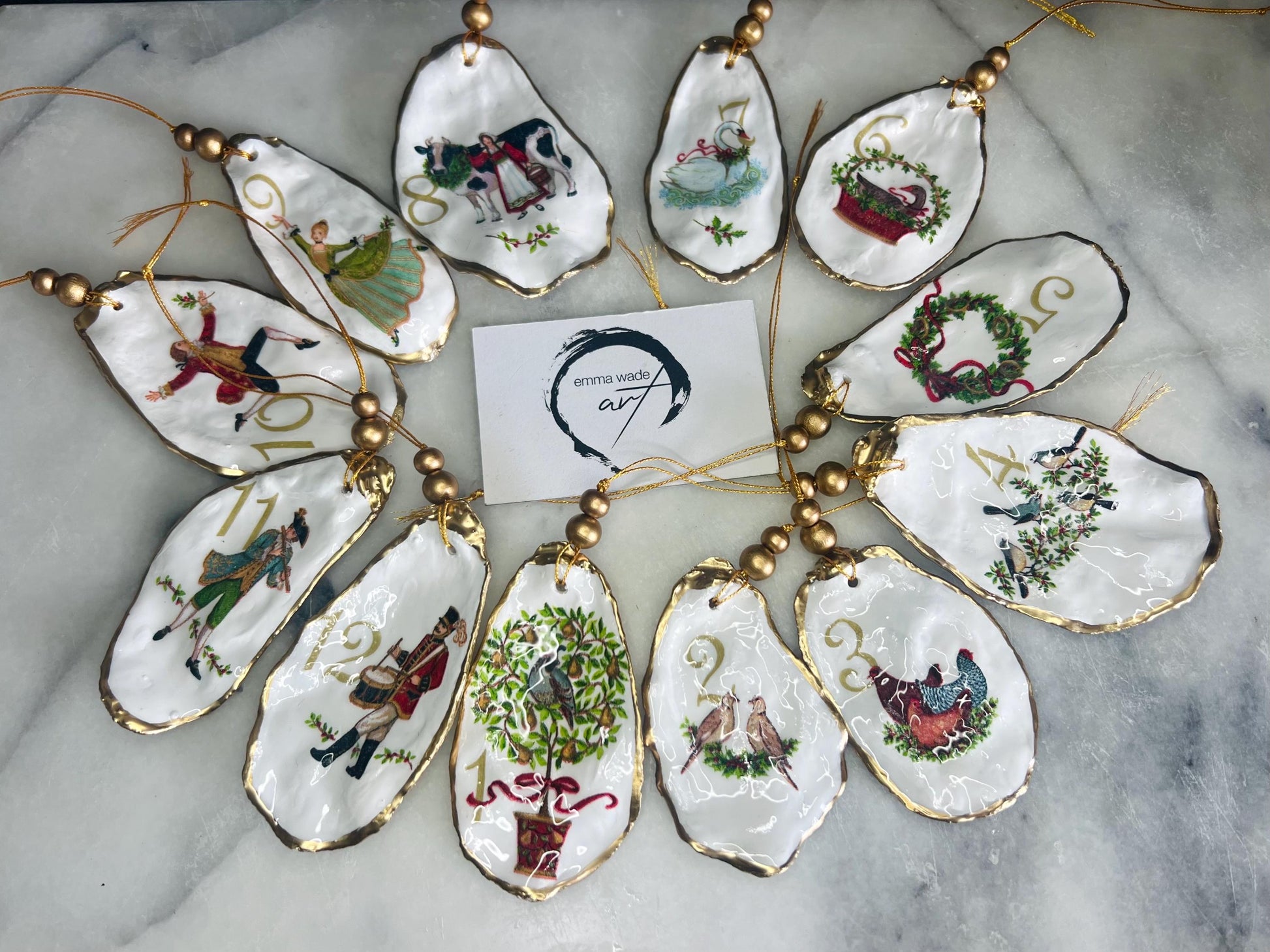 Handmade Twelve Days of Christmas oyster shell ornament set featuring all twelve traditional carol illustrations, finished with gold leaf edging, glossy resin and gold hanging cords. Coastal heirloom Christmas decorations handcrafted from Dorset oyster shells.