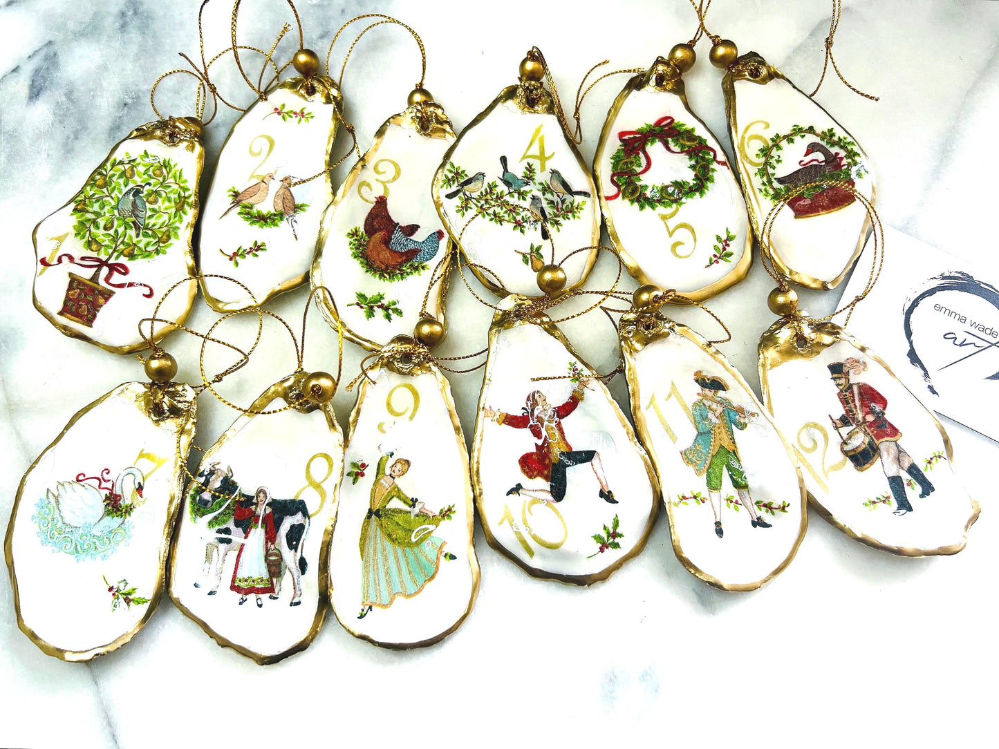 Handmade Twelve Days of Christmas oyster shell ornament set featuring all twelve traditional carol illustrations, finished with gold leaf edging, glossy resin and gold hanging cords. Coastal heirloom Christmas decorations handcrafted from Dorset oyster shells.