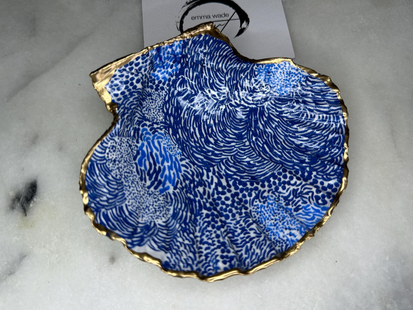 Marimekko inspired blue floral scallop shell trinket dish with hand-applied gold leaf edging and glossy resin finish. Natural Dorset shell jewellery holder featuring bold Scandinavian style botanical pattern. Decorative coastal ring dish styled on a marble surface, ideal as a bedside trinket bowl, host gift or luxury handmade home accent.