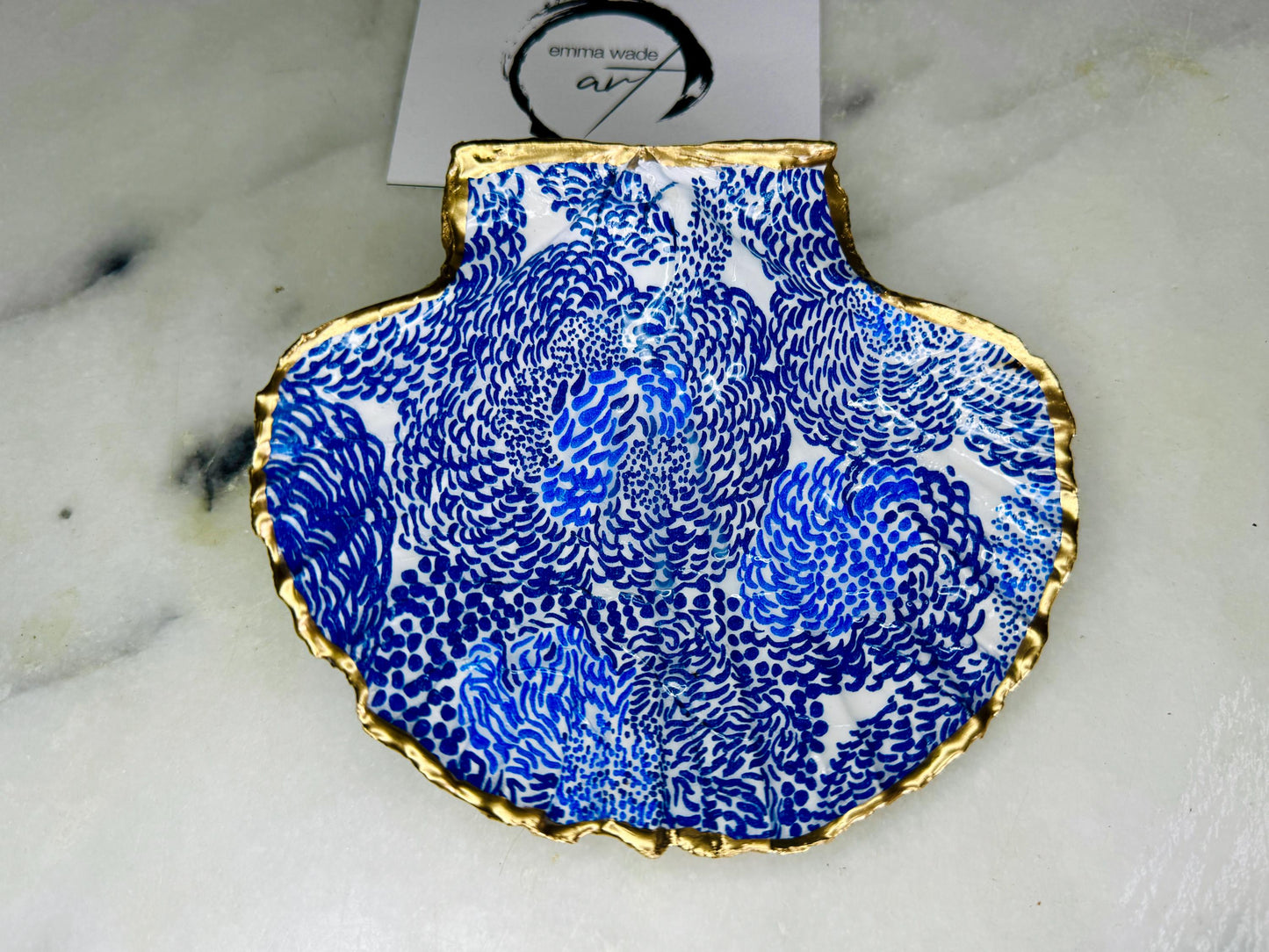 Marimekko inspired blue floral scallop shell trinket dish with hand-applied gold leaf edging and glossy resin finish. Natural Dorset shell jewellery holder featuring bold Scandinavian style botanical pattern. Decorative coastal ring dish styled on a marble surface, ideal as a bedside trinket bowl, host gift or luxury handmade home accent.