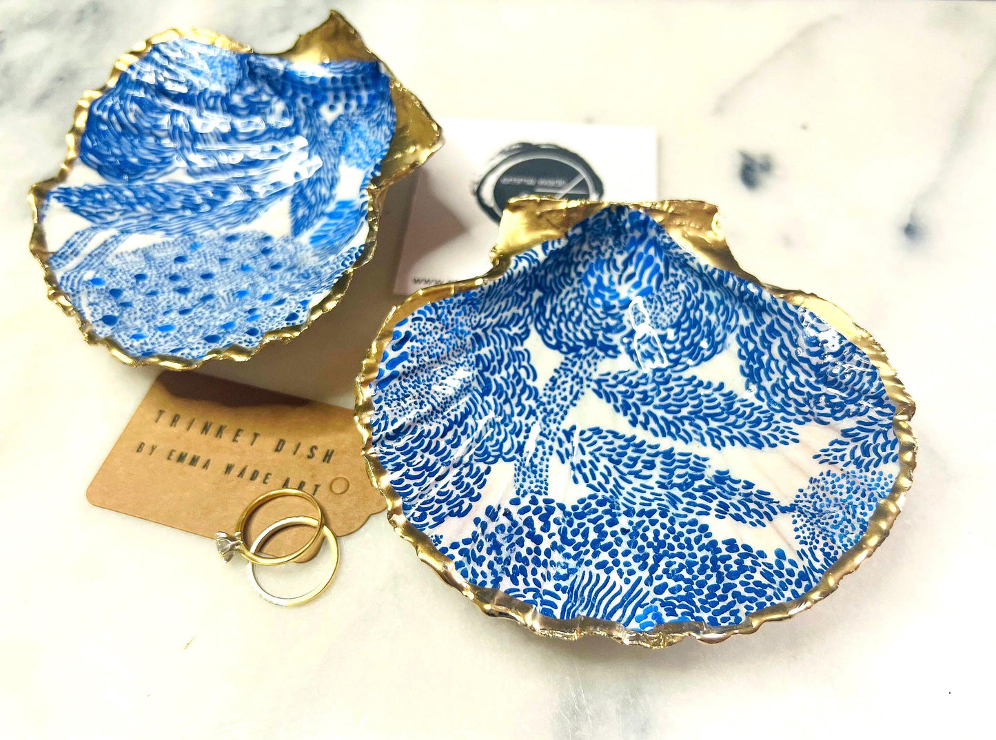 Marimekko inspired blue floral scallop shell trinket dish with hand-applied gold leaf edging and glossy resin finish. Natural Dorset shell jewellery holder featuring bold Scandinavian style botanical pattern. Decorative coastal ring dish styled on a marble surface, ideal as a bedside trinket bowl, host gift or luxury handmade home accent.