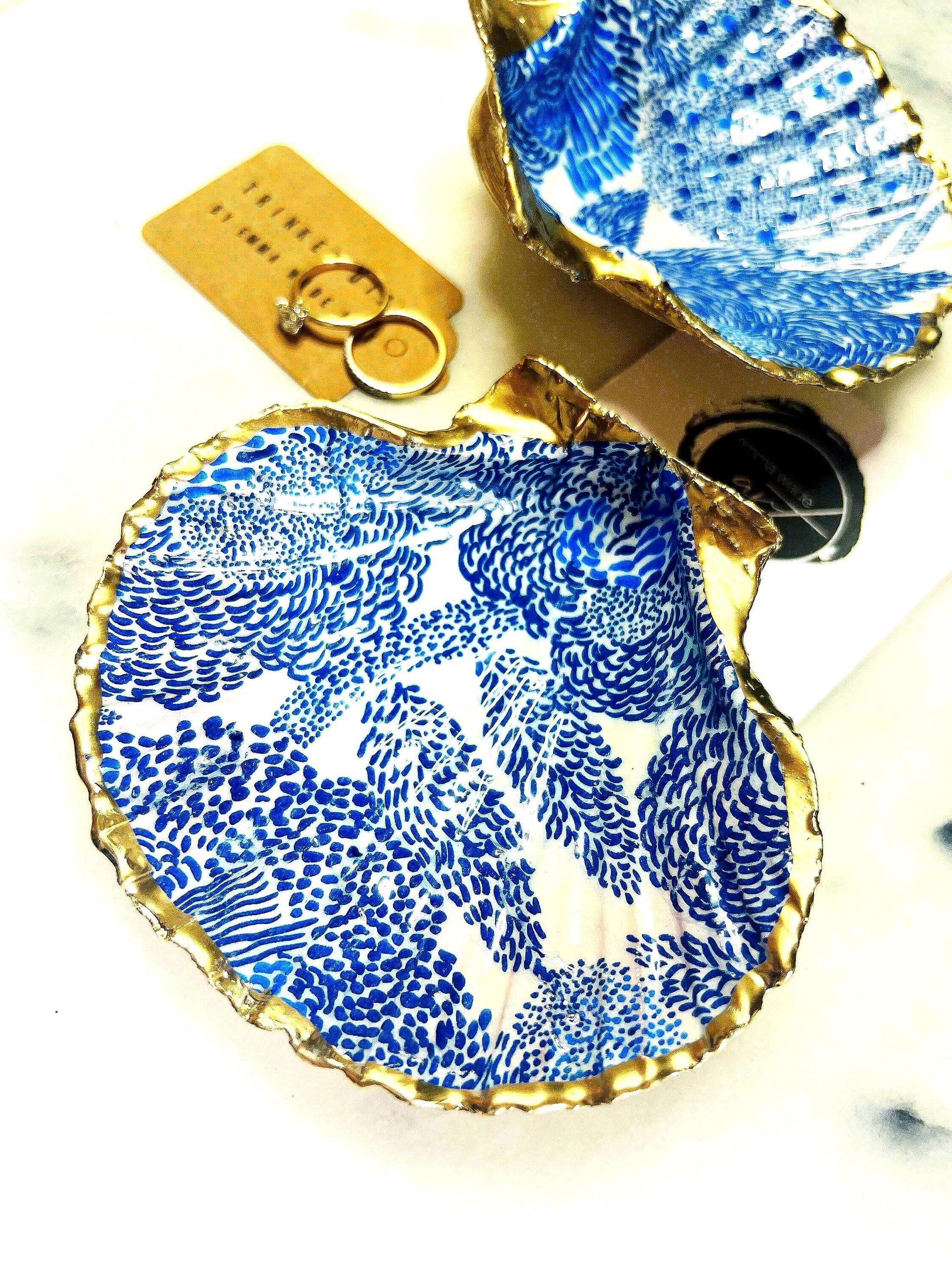 Marimekko inspired blue floral scallop shell trinket dish with hand-applied gold leaf edging and glossy resin finish. Natural Dorset shell jewellery holder featuring bold Scandinavian style botanical pattern. Decorative coastal ring dish styled on a marble surface, ideal as a bedside trinket bowl, host gift or luxury handmade home accent.