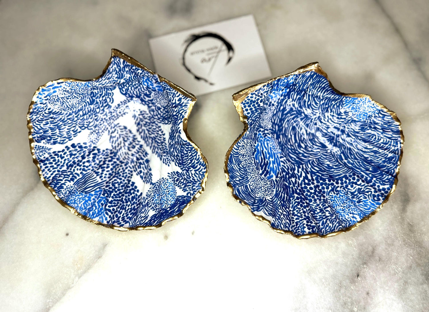 Marimekko inspired blue floral scallop shell trinket dish with hand-applied gold leaf edging and glossy resin finish. Natural Dorset shell jewellery holder featuring bold Scandinavian style botanical pattern. Decorative coastal ring dish styled on a marble surface, ideal as a bedside trinket bowl, host gift or luxury handmade home accent.