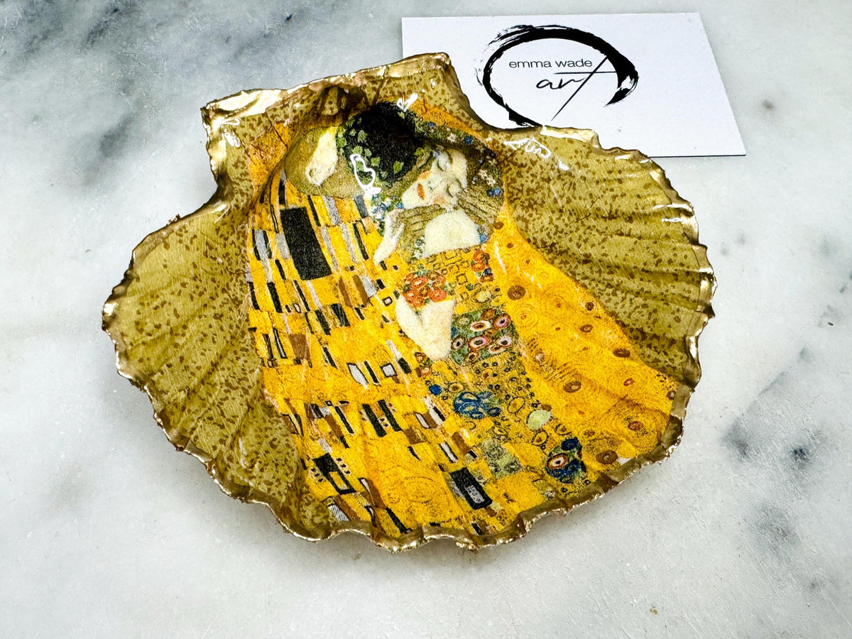 Handmade scallop shell trinket dish inspired by Gustav Klimt’s “The Kiss”, finished with gold leaf and sealed with glossy resin. Coastal Dorset shell jewellery dish perfect for rings, earrings and small treasures. Unique decorative shell bowl with golden artwork design, photographed on a light background showing detailed gilded surface and natural shell shape.