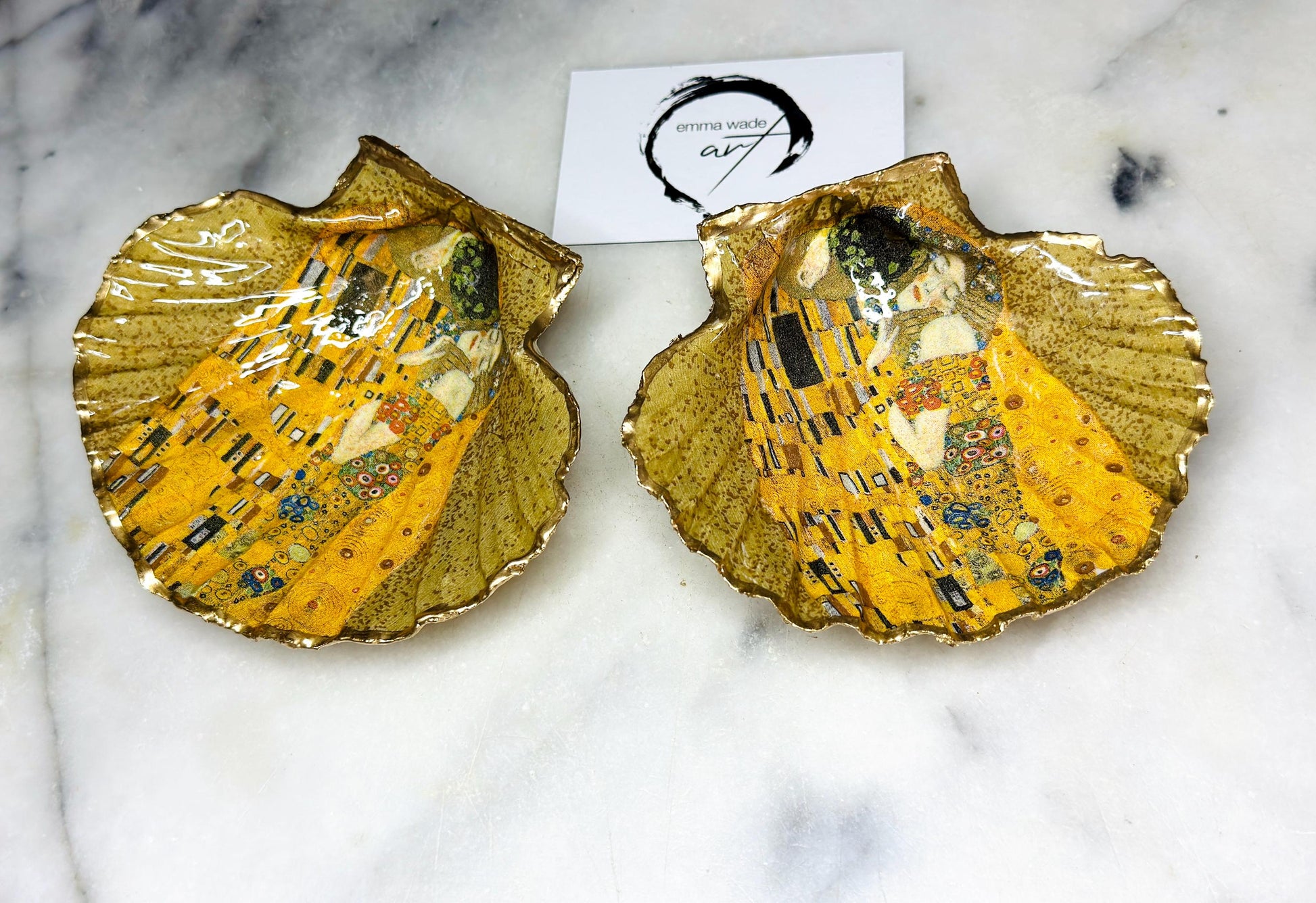 Handmade scallop shell trinket dish inspired by Gustav Klimt’s “The Kiss”, finished with gold leaf and sealed with glossy resin. Coastal Dorset shell jewellery dish perfect for rings, earrings and small treasures. Unique decorative shell bowl with golden artwork design, photographed on a light background showing detailed gilded surface and natural shell shape.