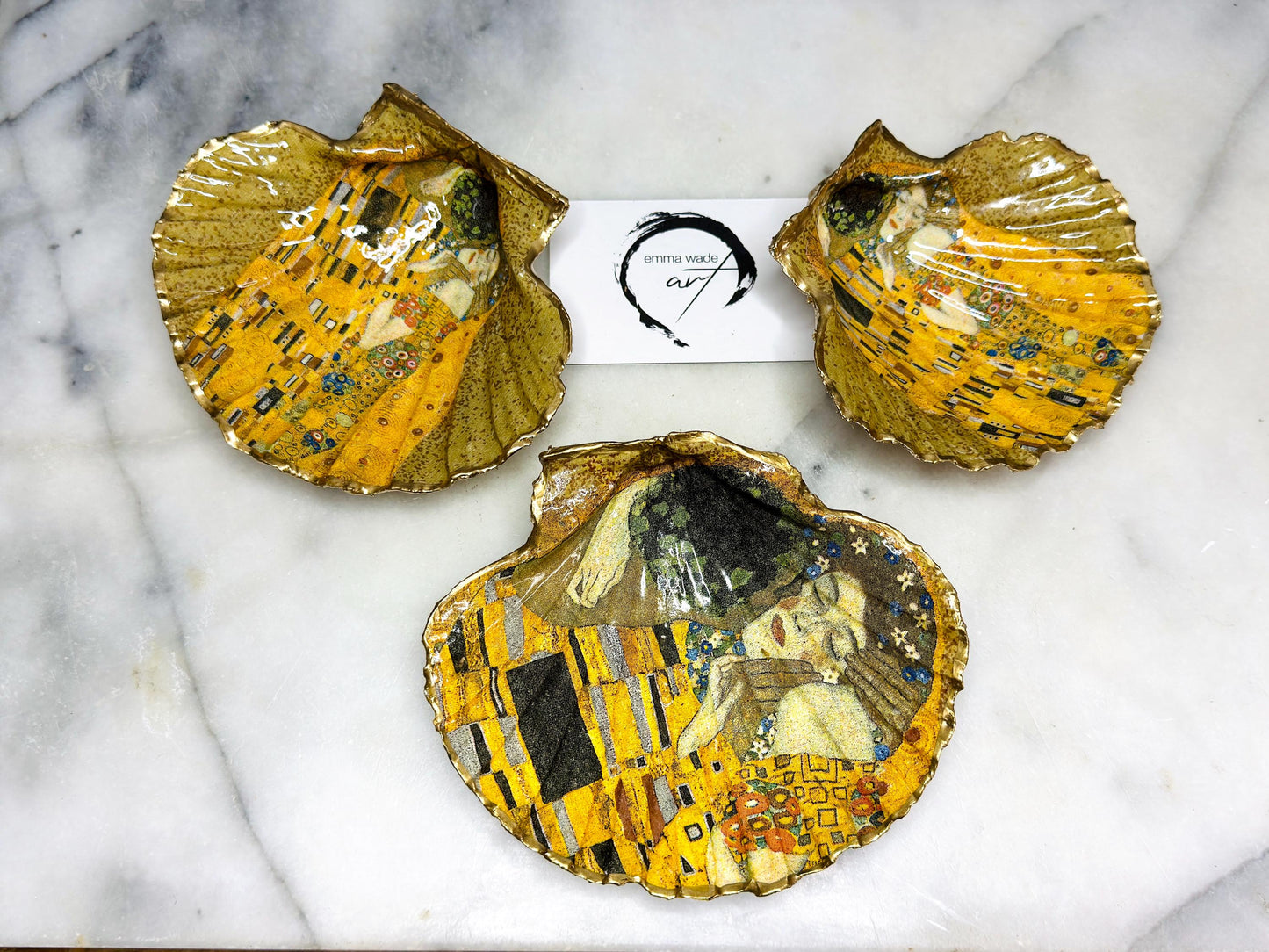 Handmade scallop shell trinket dish inspired by Gustav Klimt’s “The Kiss”, finished with gold leaf and sealed with glossy resin. Coastal Dorset shell jewellery dish perfect for rings, earrings and small treasures. Unique decorative shell bowl with golden artwork design, photographed on a light background showing detailed gilded surface and natural shell shape.