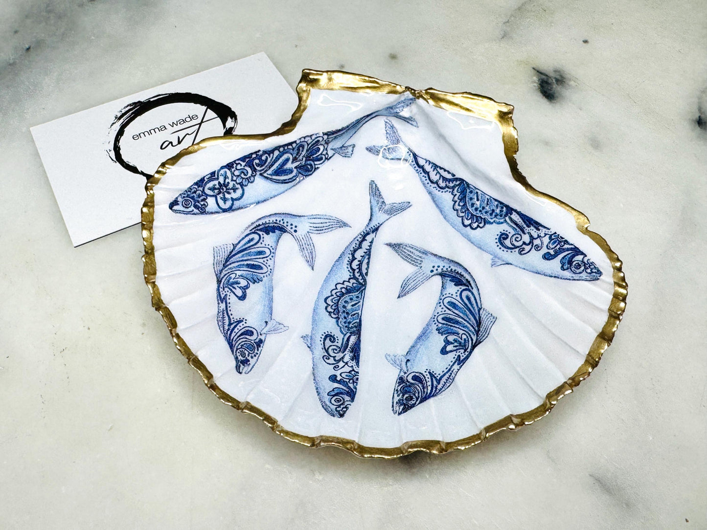 Handmade Dorset scallop shell trinket dishes featuring blue and white paisley fish illustrations with hand-painted gold leaf edging and glossy crystal clear resin. Coastal Scandinavian inspired jewellery dishes styled on a soft neutral background with elegant nautical fish artwork and luxurious gilded detailing.