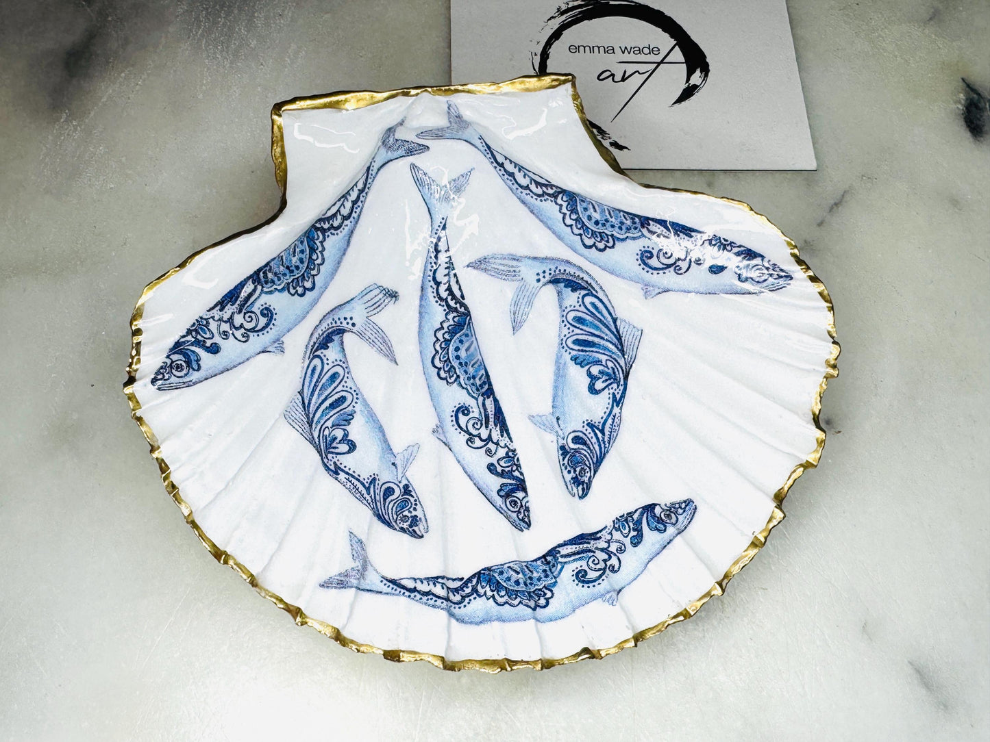 Handmade Dorset scallop shell trinket dishes featuring blue and white paisley fish illustrations with hand-painted gold leaf edging and glossy crystal clear resin. Coastal Scandinavian inspired jewellery dishes styled on a soft neutral background with elegant nautical fish artwork and luxurious gilded detailing.