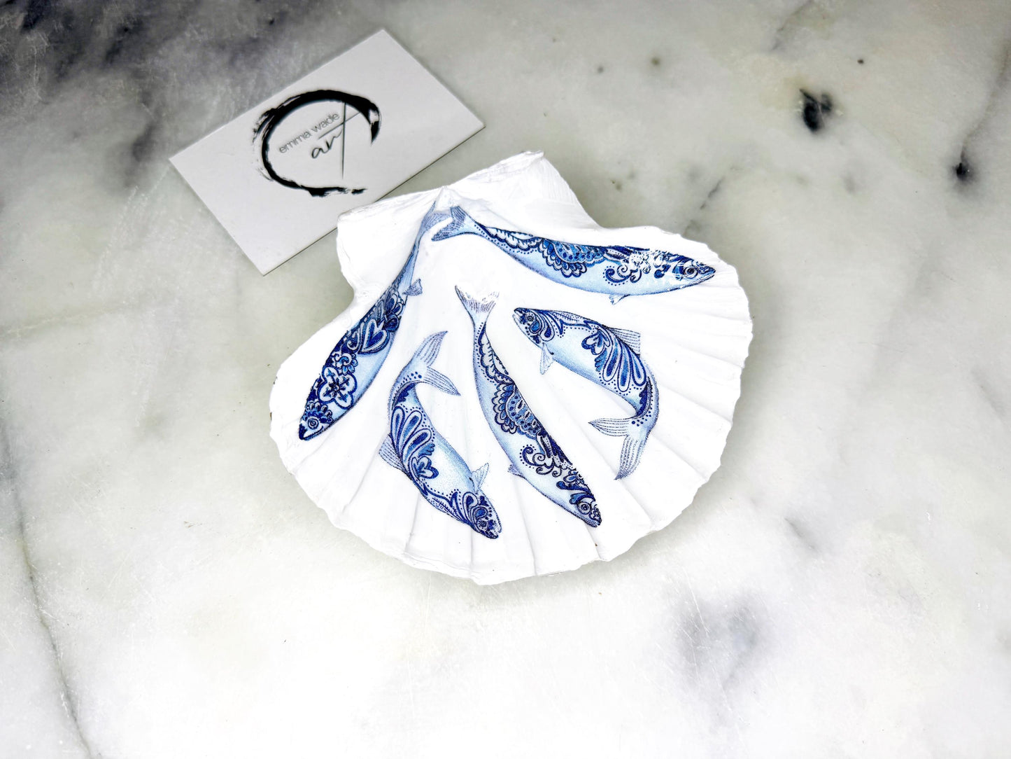 Handmade Dorset scallop shell trinket dishes featuring blue and white paisley fish illustrations with hand-painted gold leaf edging and glossy crystal clear resin. Coastal Scandinavian inspired jewellery dishes styled on a soft neutral background with elegant nautical fish artwork and luxurious gilded detailing.