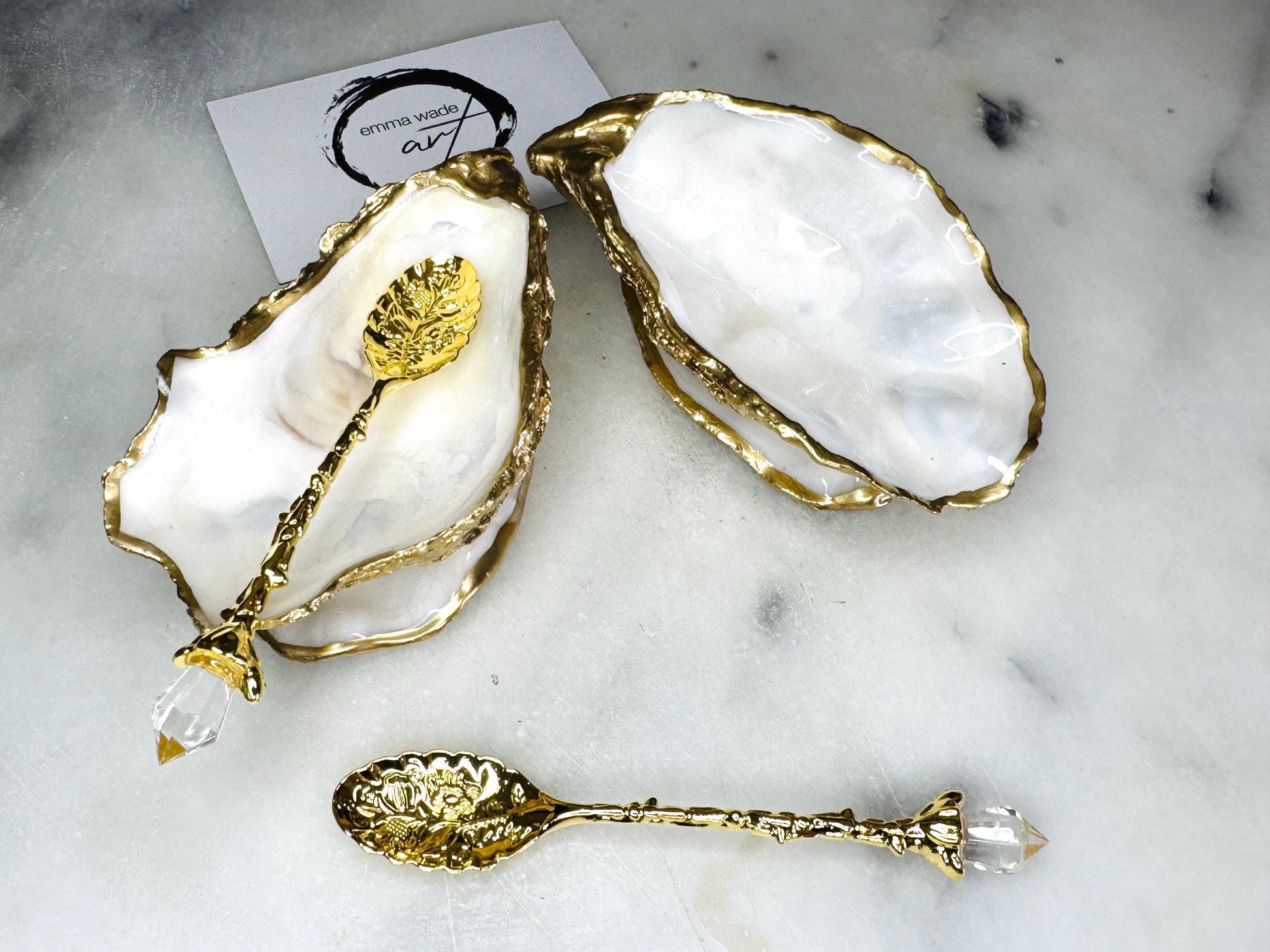 Handmade gold leaf oyster shell salt cellar set with pearl interiors and matching spoons. Coastal pinch pots made from Dorset oyster shells, sealed with glossy resin and finished with gilded edges. Luxury tableware set photographed on a light background, showing two shell salt dishes and decorative spoons, perfect for serving salt or spices at the table.
