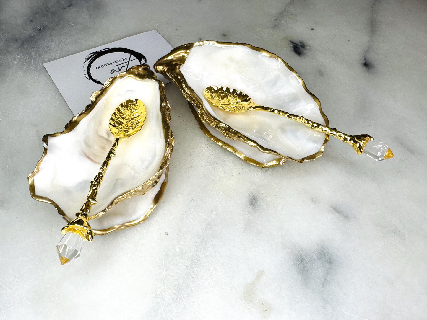 Handmade gold leaf oyster shell salt cellar set with pearl interiors and matching spoons. Coastal pinch pots made from Dorset oyster shells, sealed with glossy resin and finished with gilded edges. Luxury tableware set photographed on a light background, showing two shell salt dishes and decorative spoons, perfect for serving salt or spices at the table.