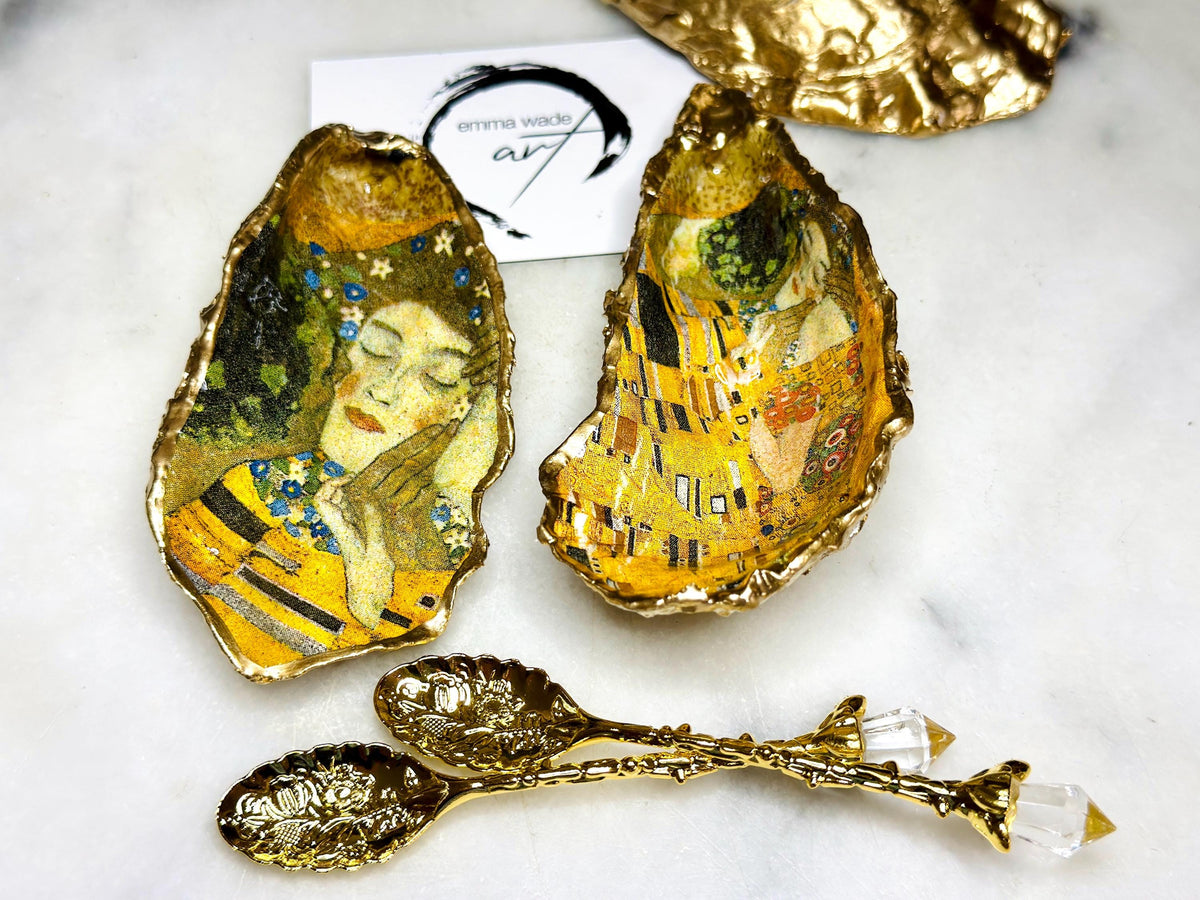Pair of handmade Dorset oyster shell salt and pepper pinch pots inspired by Gustav Klimt’s The Kiss, decorated with rich gold artwork, hand-finished with liquid gold leaf, and sealed in crystal-hard glossy resin. Luxury coastal serving dishes with optional gold crystal spoons, perfect for weddings, anniversaries, dinner parties, and elegant table décor.
