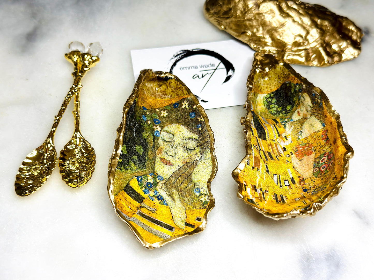 Pair of handmade Dorset oyster shell salt and pepper pinch pots inspired by Gustav Klimt’s The Kiss, decorated with rich gold artwork, hand-finished with liquid gold leaf, and sealed in crystal-hard glossy resin. Luxury coastal serving dishes with optional gold crystal spoons, perfect for weddings, anniversaries, dinner parties, and elegant table décor.