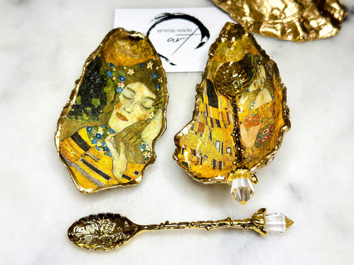 Pair of handmade Dorset oyster shell salt and pepper pinch pots inspired by Gustav Klimt’s The Kiss, decorated with rich gold artwork, hand-finished with liquid gold leaf, and sealed in crystal-hard glossy resin. Luxury coastal serving dishes with optional gold crystal spoons, perfect for weddings, anniversaries, dinner parties, and elegant table décor.