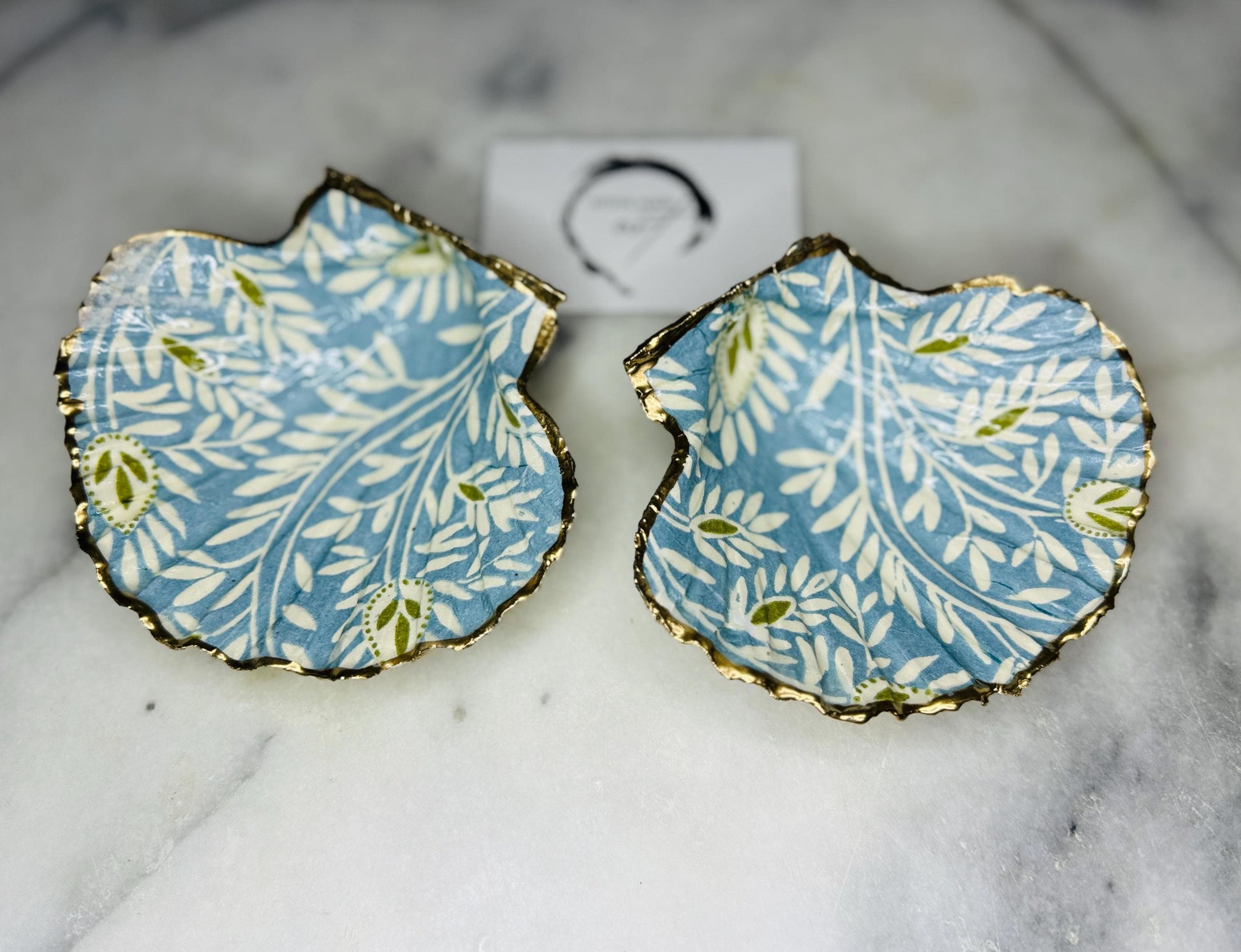 Elegant Blue Green floral scallop shell trinket dish, hand-painted and gilded with liquid gold leaf before being sealed in crystal-clear resin. Each shell is a one-of-a-kind Dorset creation, perfect as a jewellery holder, tea light dish, or coastal home décor accent. A beautiful handmade ocean-inspired gift, presented in eco-friendly packaging and finished with sustainable care and artistry