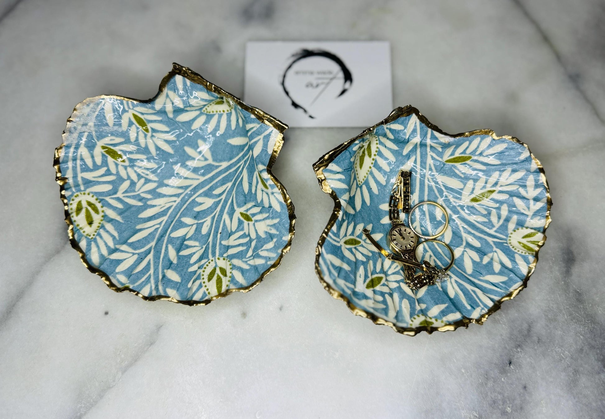 Handcrafted Blue and Green floral scallop shell trinket dish, gilded with liquid gold leaf and sealed in resin. Inspired by the Dorset coastline, this unique jewellery holder or trinket bowl is made from an authentic scallop shell and presented in a sustainable gift box. A thoughtful handmade coastal décor piece and ocean lover gift, ideal for weddings, birthdays, or elegant home styling.