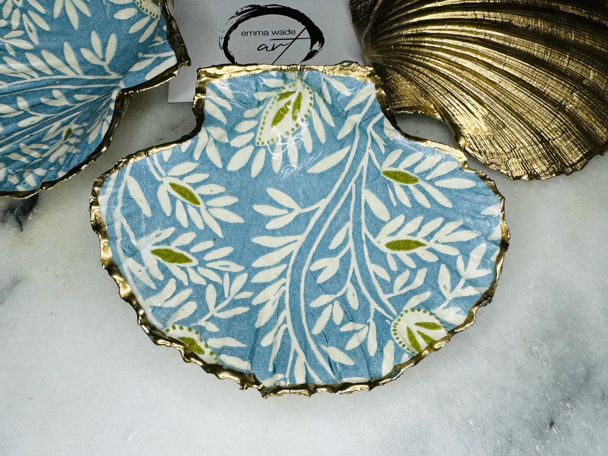 Handcrafted Blue and Green floral scallop shell trinket dish, gilded with liquid gold leaf and sealed in resin. Inspired by the Dorset coastline, this unique jewellery holder or trinket bowl is made from an authentic scallop shell and presented in a sustainable gift box. A thoughtful handmade coastal décor piece and ocean lover gift, ideal for weddings, birthdays, or elegant home styling.