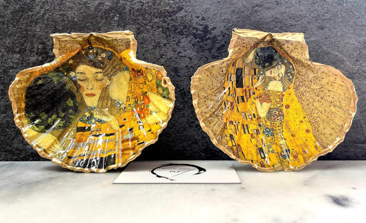 Handmade scallop shell trinket dish inspired by Gustav Klimt’s “The Kiss”, finished with gold leaf and sealed with glossy resin. Coastal Dorset shell jewellery dish perfect for rings, earrings and small treasures. Unique decorative shell bowl with golden artwork design, photographed on a light background showing detailed gilded surface and natural shell shape.