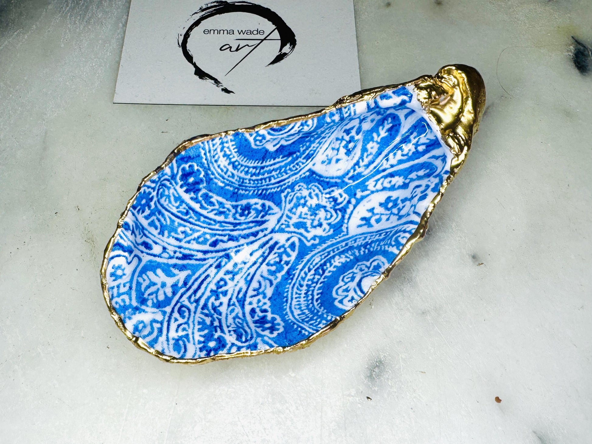 Blue and white paisley oyster shell salt cellar set with gold leaf edging and matching gold crystal spoons. Handmade Dorset oyster shell pinch pots finished in glossy food safe resin. Coastal dining decor and luxury beach house table accessory.