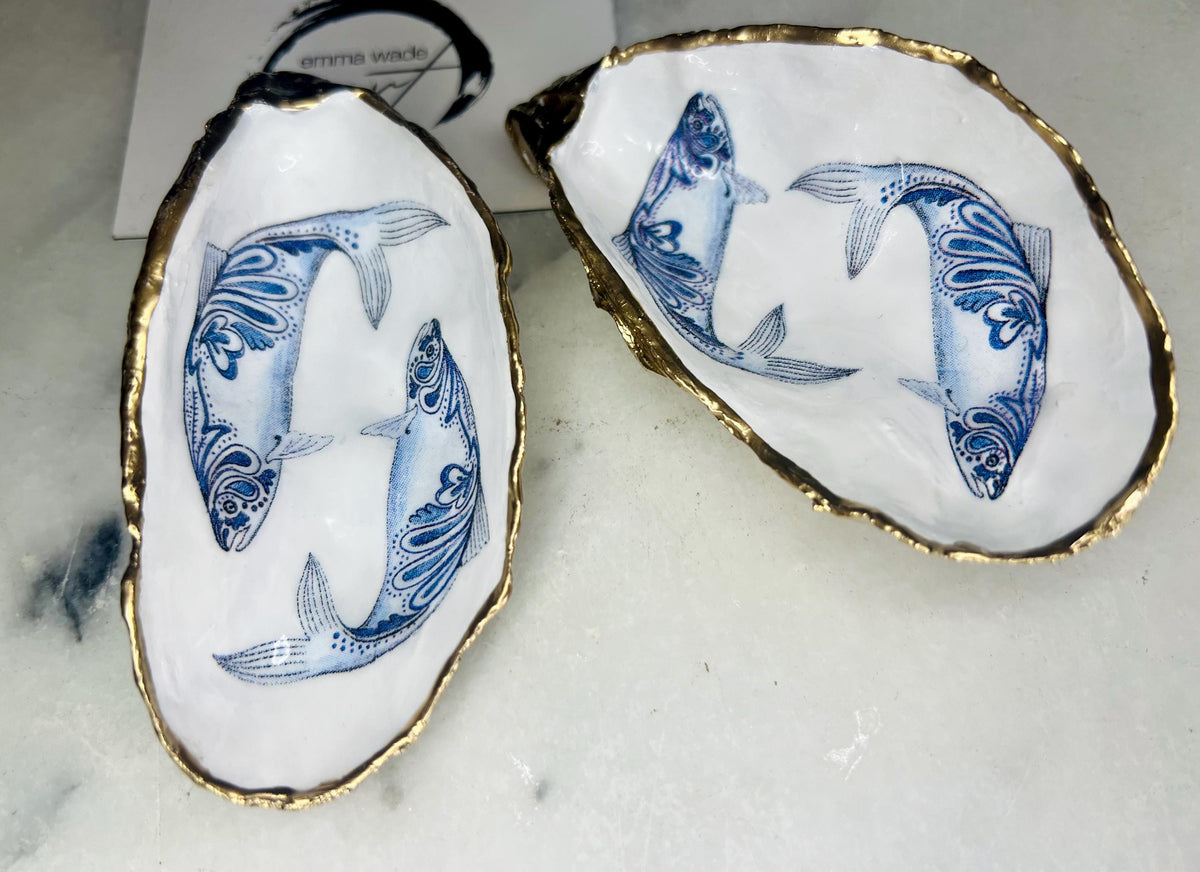 Handmade Dorset oyster shell trinket dish with blue and white paisley fish design, gold leaf gilded edges and glossy resin finish. Coastal jewellery holder and ring dish, photographed on a light surface showing the natural shell shape and pearly interior. Unique sustainably sourced shell, sold individually as a decorative coastal home décor accent or gift.