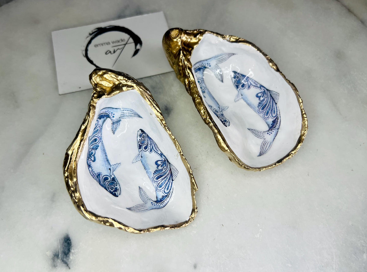 Handmade Dorset oyster shell trinket dish with blue and white paisley fish design, gold leaf gilded edges and glossy resin finish. Coastal jewellery holder and ring dish, photographed on a light surface showing the natural shell shape and pearly interior. Unique sustainably sourced shell, sold individually as a decorative coastal home décor accent or gift.