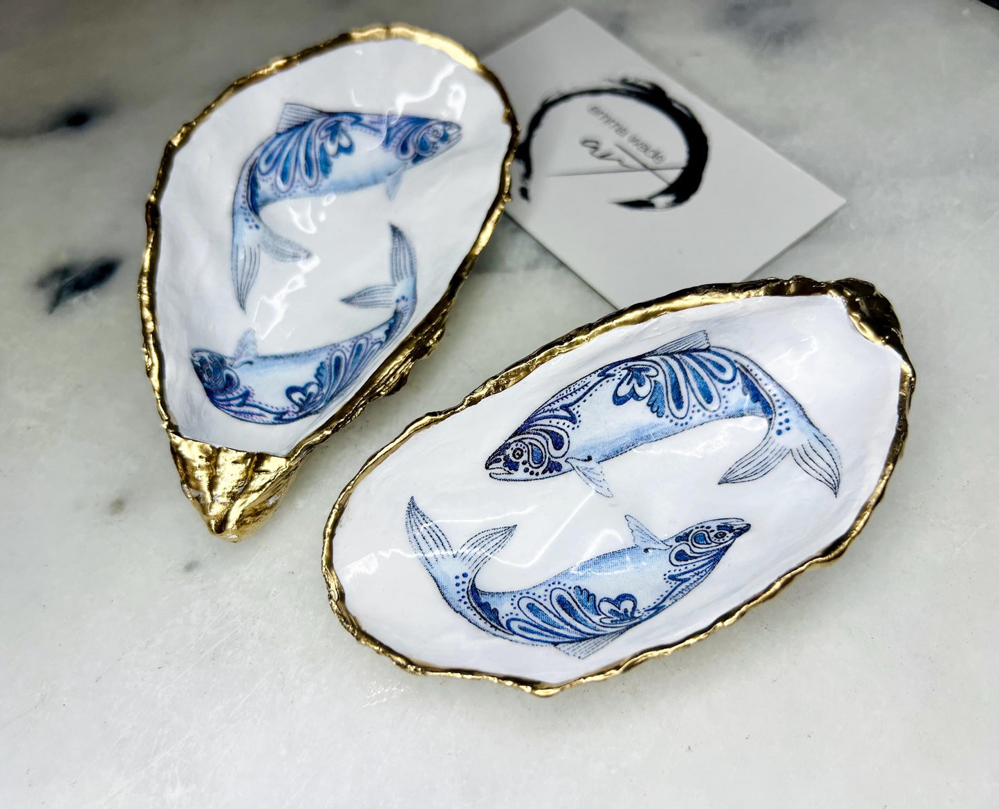 Handmade Dorset oyster shell trinket dish with blue and white paisley fish design, gold leaf gilded edges and glossy resin finish. Coastal jewellery holder and ring dish, photographed on a light surface showing the natural shell shape and pearly interior. Unique sustainably sourced shell, sold individually as a decorative coastal home décor accent or gift.