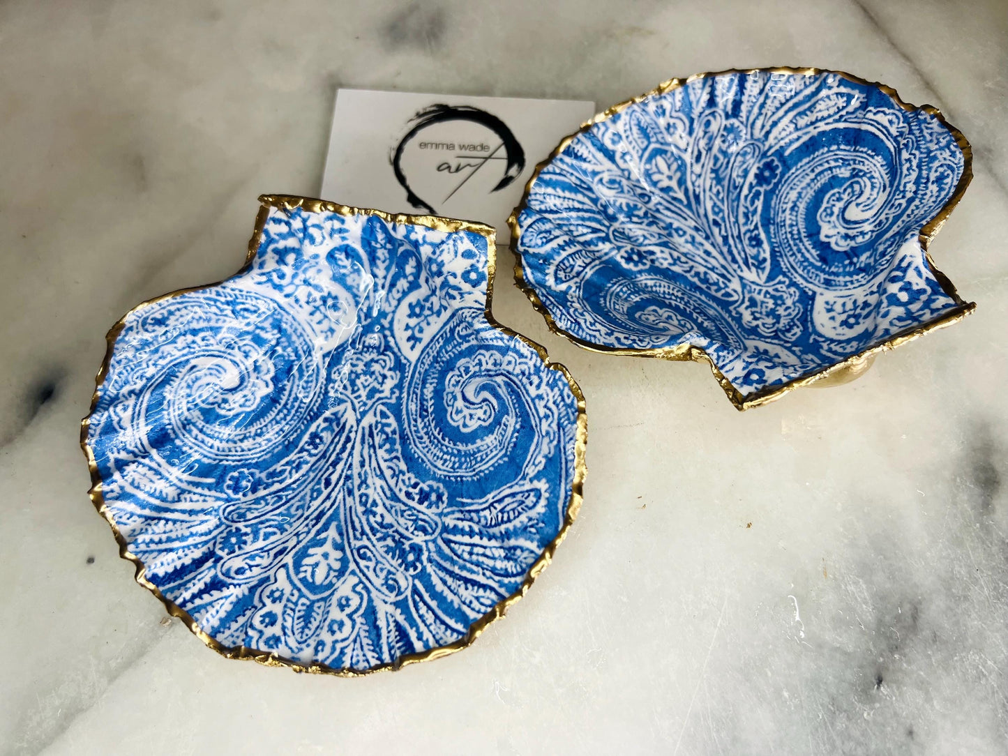 Blue and white paisley scallop shell ring catcher with hand applied gold leaf edging and glossy resin finish. Handmade Dorset shell jewellery tray styled with pearls on a marble background. Coastal vanity decor and luxury beach house accessory gift.