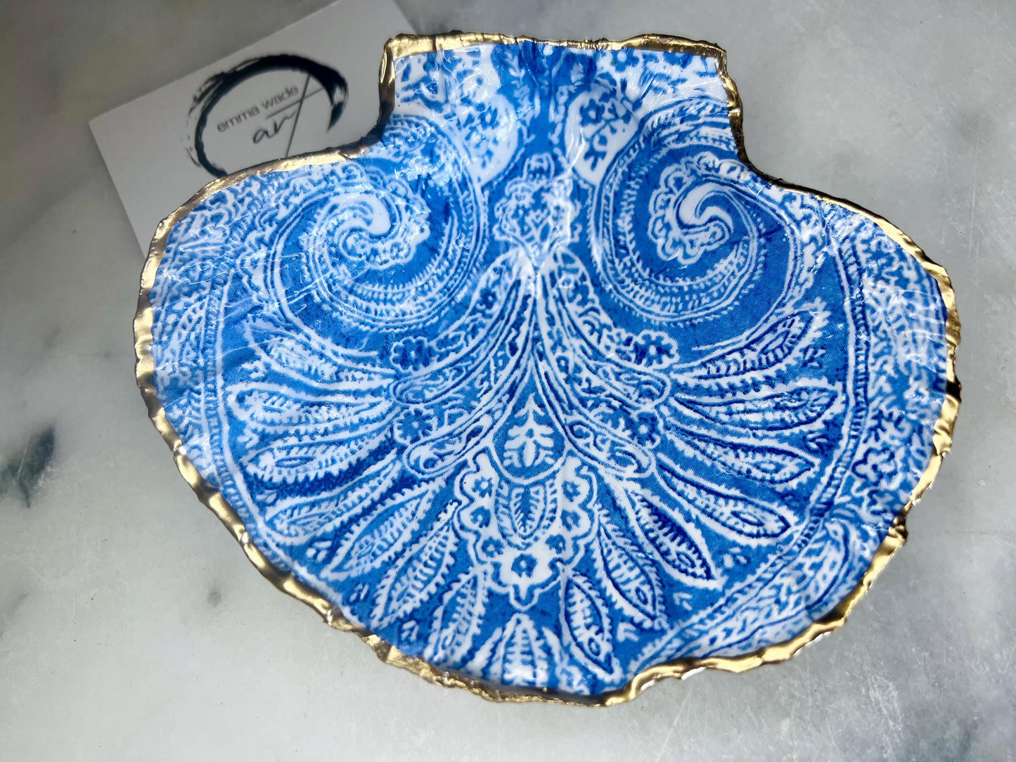 Blue and white paisley scallop shell ring catcher with hand applied gold leaf edging and glossy resin finish. Handmade Dorset shell jewellery tray styled with pearls on a marble background. Coastal vanity decor and luxury beach house accessory gift.