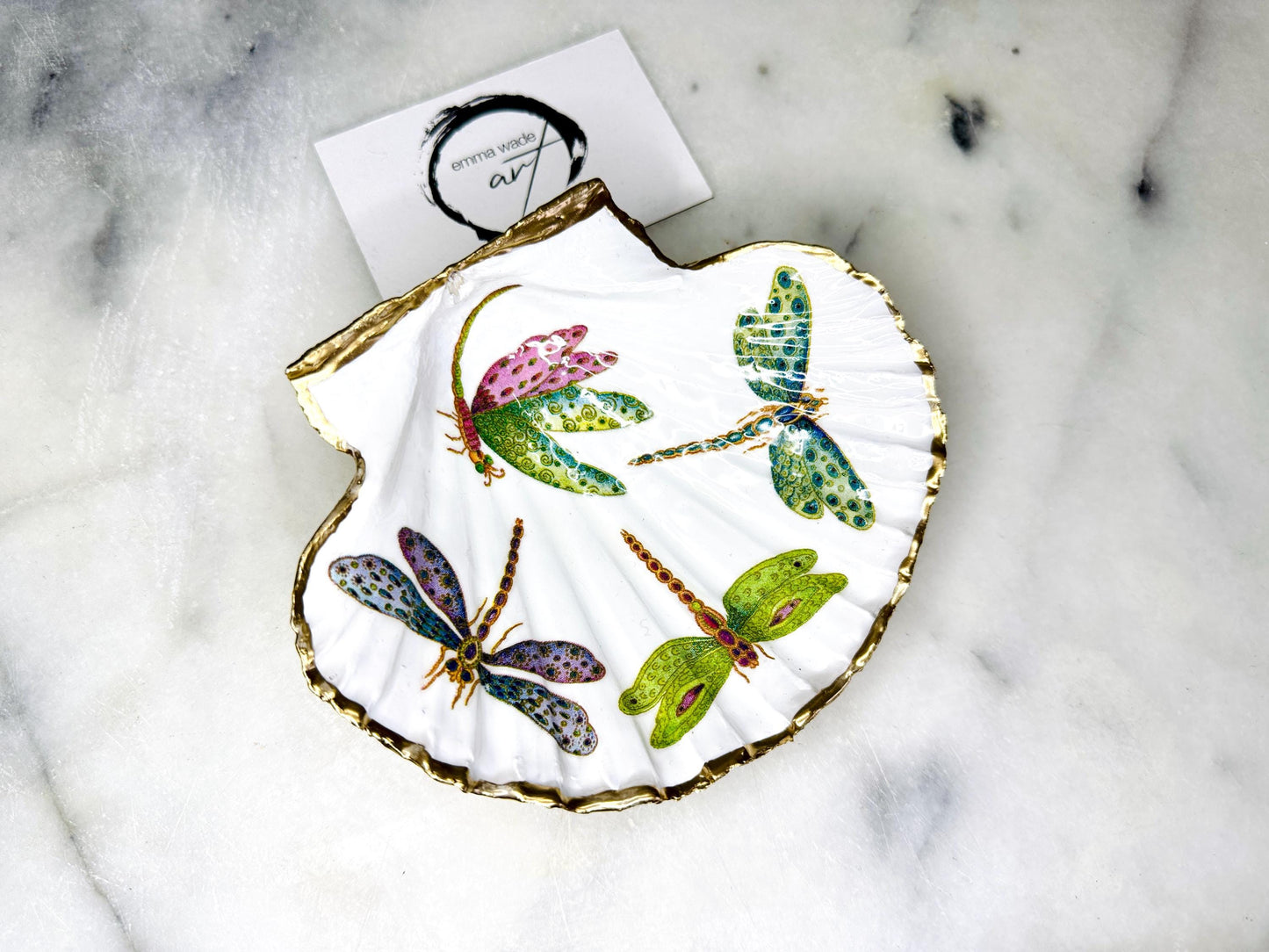 Handmade dragonfly scallop shell trinket dish with gold leaf edging and glossy resin finish. Coastal jewellery and ring dish crafted from a natural Dorset scallop shell, featuring colourful dragonfly artwork. Decorative shell bowl photographed on a light background, showing the natural shell shape and shimmering gilded edges, ideal for holding rings, earrings, trinkets or small treasures.