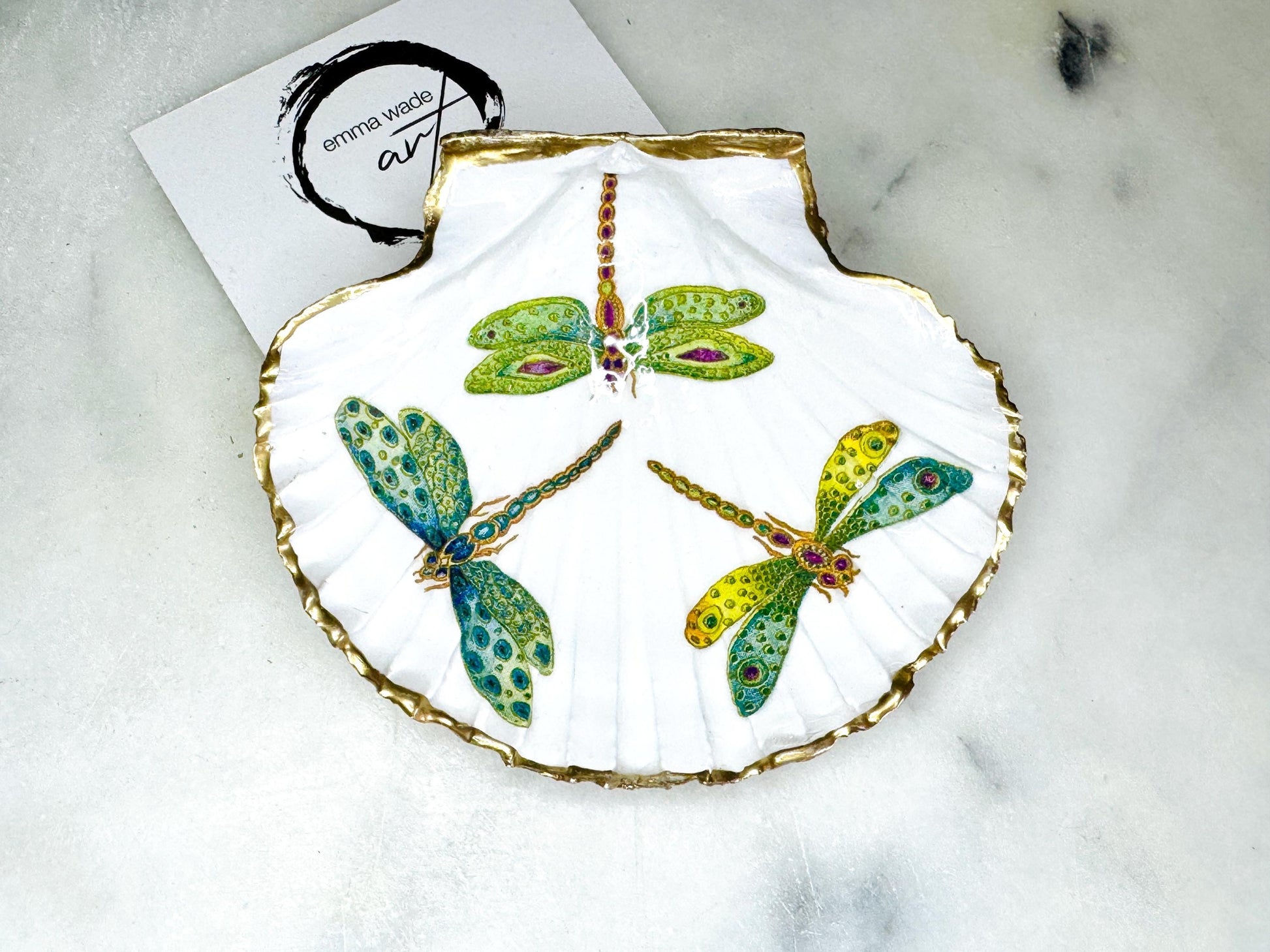 Handmade dragonfly scallop shell trinket dish with gold leaf edging and glossy resin finish. Coastal jewellery and ring dish crafted from a natural Dorset scallop shell, featuring colourful dragonfly artwork. Decorative shell bowl photographed on a light background, showing the natural shell shape and shimmering gilded edges, ideal for holding rings, earrings, trinkets or small treasures.