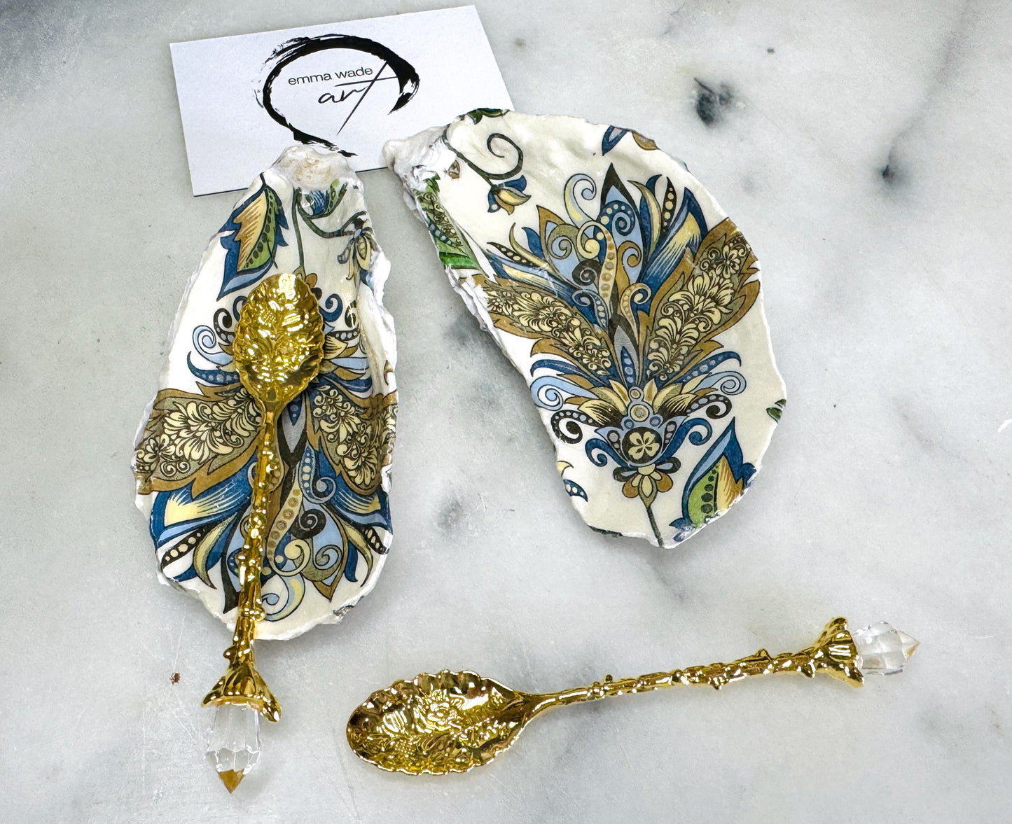 Handmade oyster shell salt and pepper dishes decorated in an elegant baroque gold design, shown as a matching pair with two gold spoons on a light marble background. Natural Dorset shells turned into coastal-inspired pinch pots, perfect for luxury table decor, wedding tables, or a unique hostess gift. Each shell is individually crafted, glossy finished, and one of a kind.